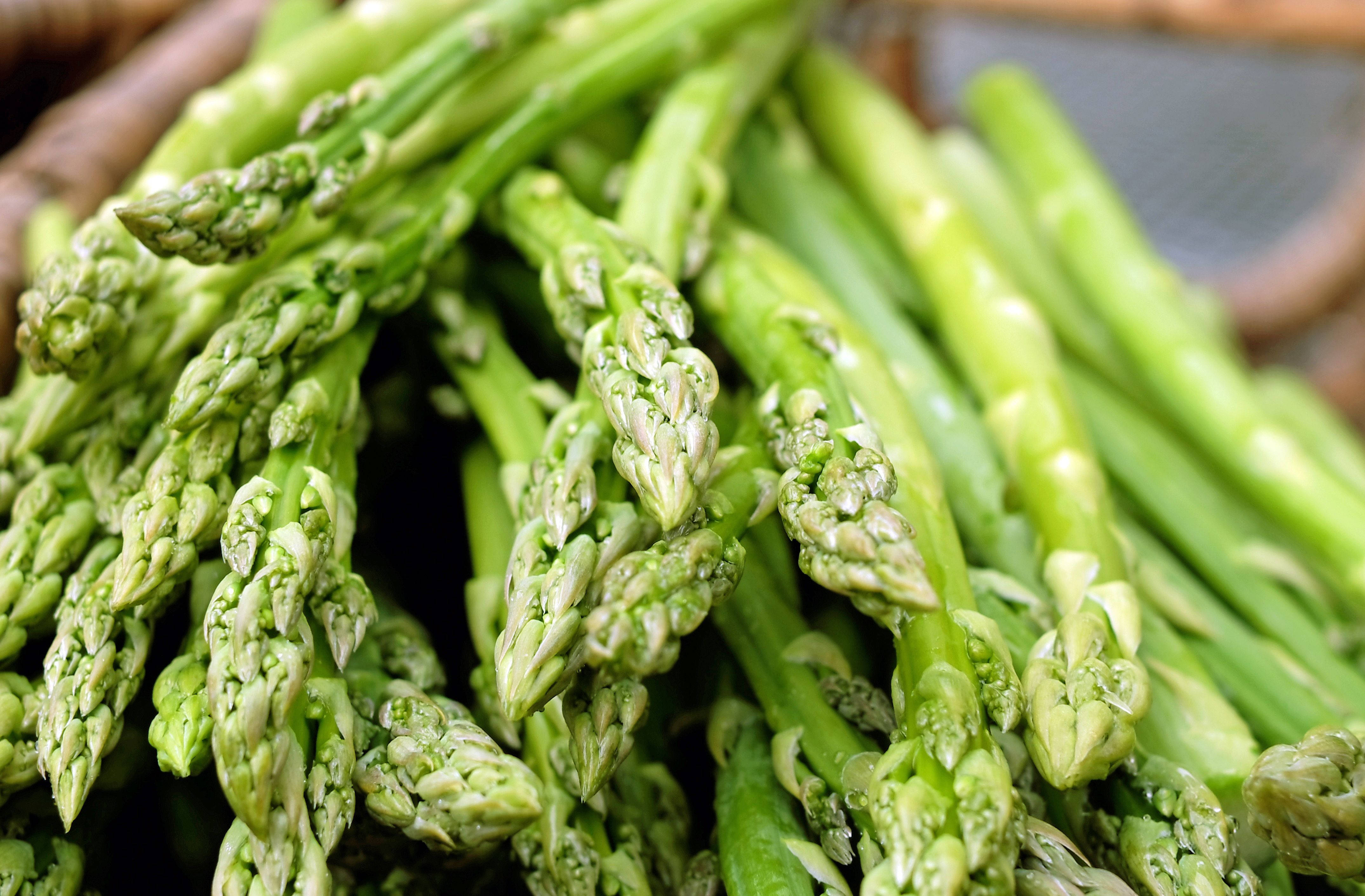 Healthy Food 桌布 壁紙 — 新鮮翠綠的蘆筍尖端帶有露珠，堆疊在編織籃中的特寫。