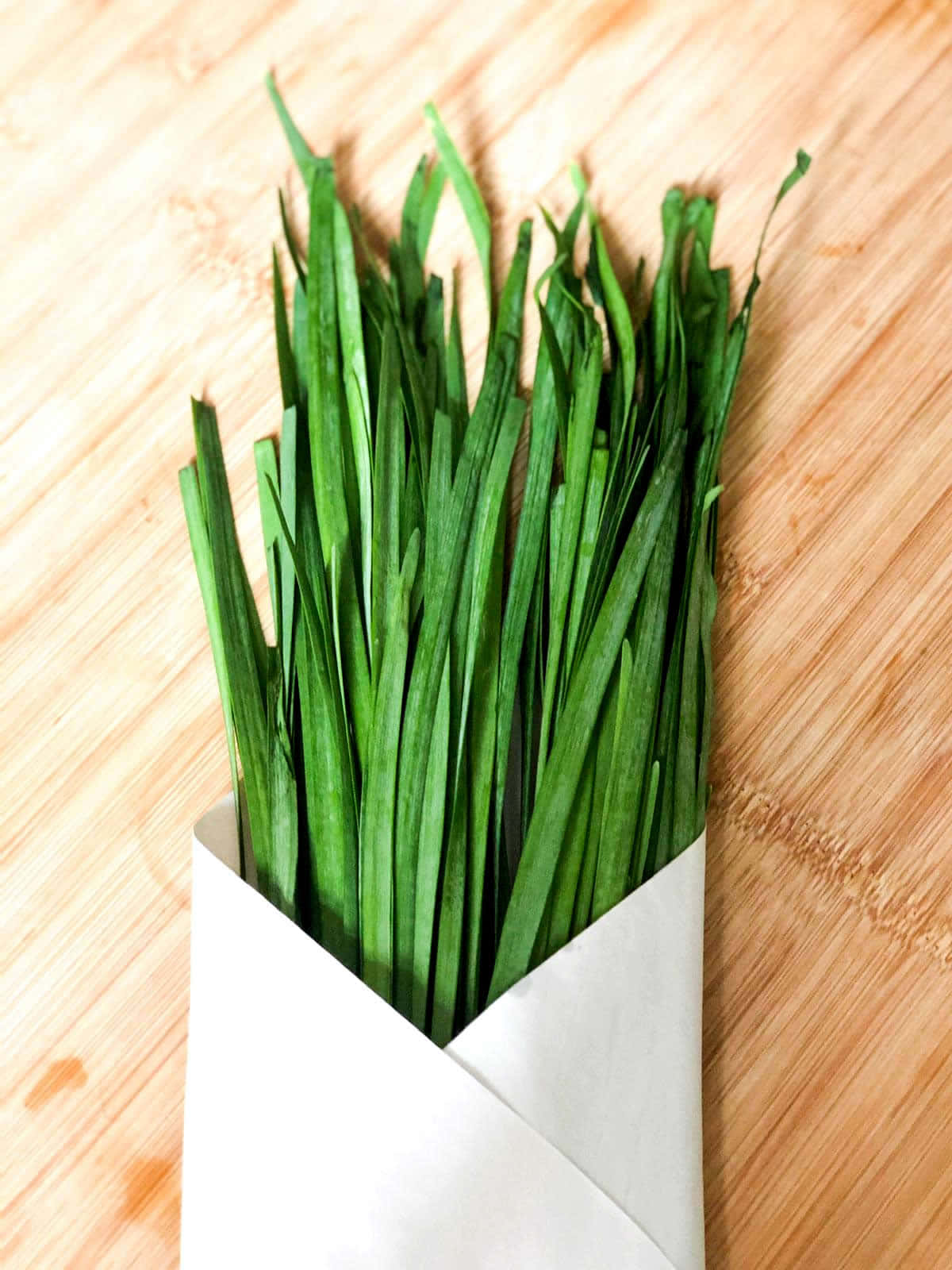 Food Photography 桌布 壁紙 — 新鮮翠綠的韭菜用白紙捆紮，放在溫暖的木砧板上。