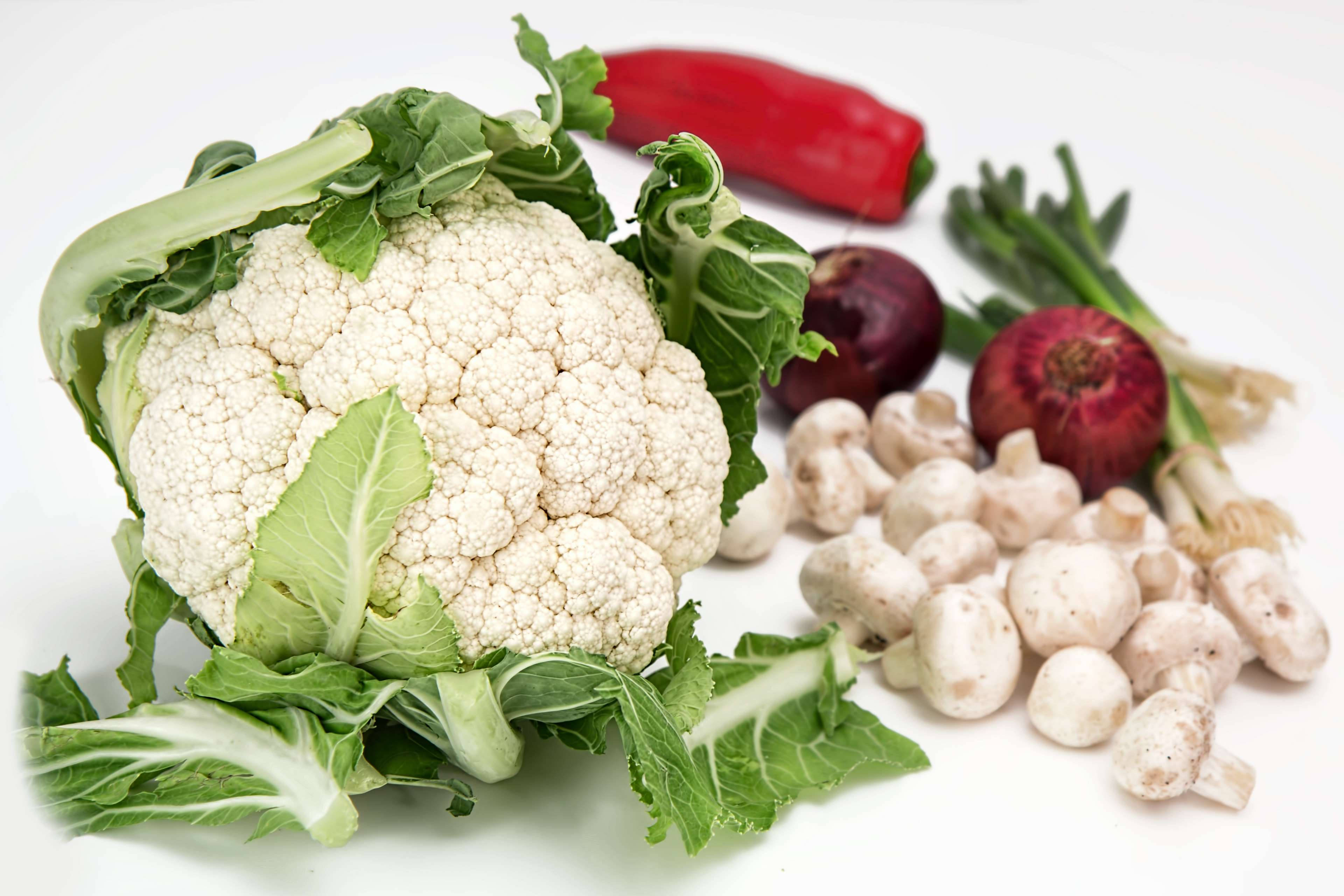Vegetables 桌布 壁紙 — 新鮮花椰菜搭配綠葉，周圍有蘑菇、紅辣椒和紅洋蔥，放在白色背景上。