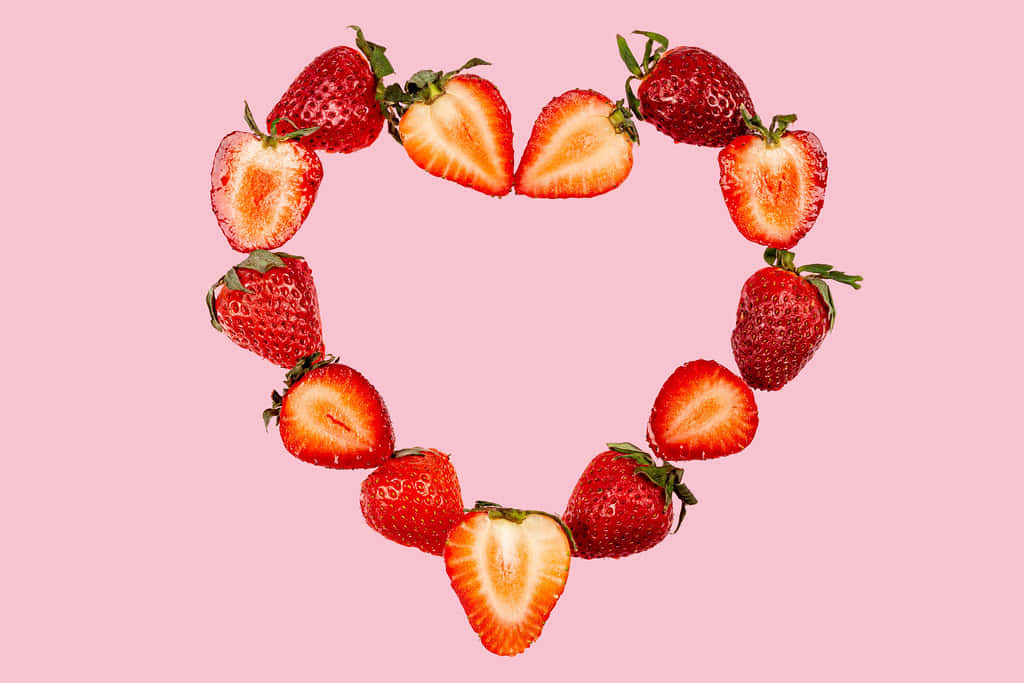 Strawberries 桌布 壁紙 — 新鮮草莓切成兩半，在柔和的粉紅色背景上形成鮮明的心形。