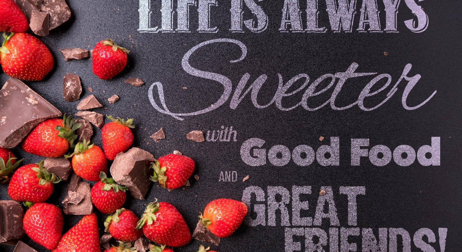 Strawberry Aesthetic 桌布 壁紙 — 新鮮草莓和巧克力塊圍繞著一塊黑板，上面寫著「生活因美食和好友而更甜蜜」。