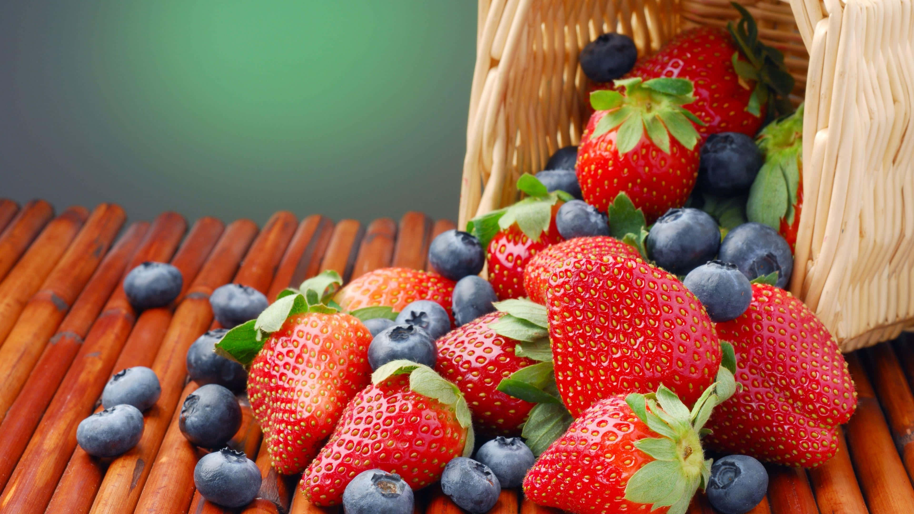 Fruits 桌布 壁紙 — 新鮮草莓和藍莓從編織籃子溢出到竹蓆上，背景為柔和綠色。
