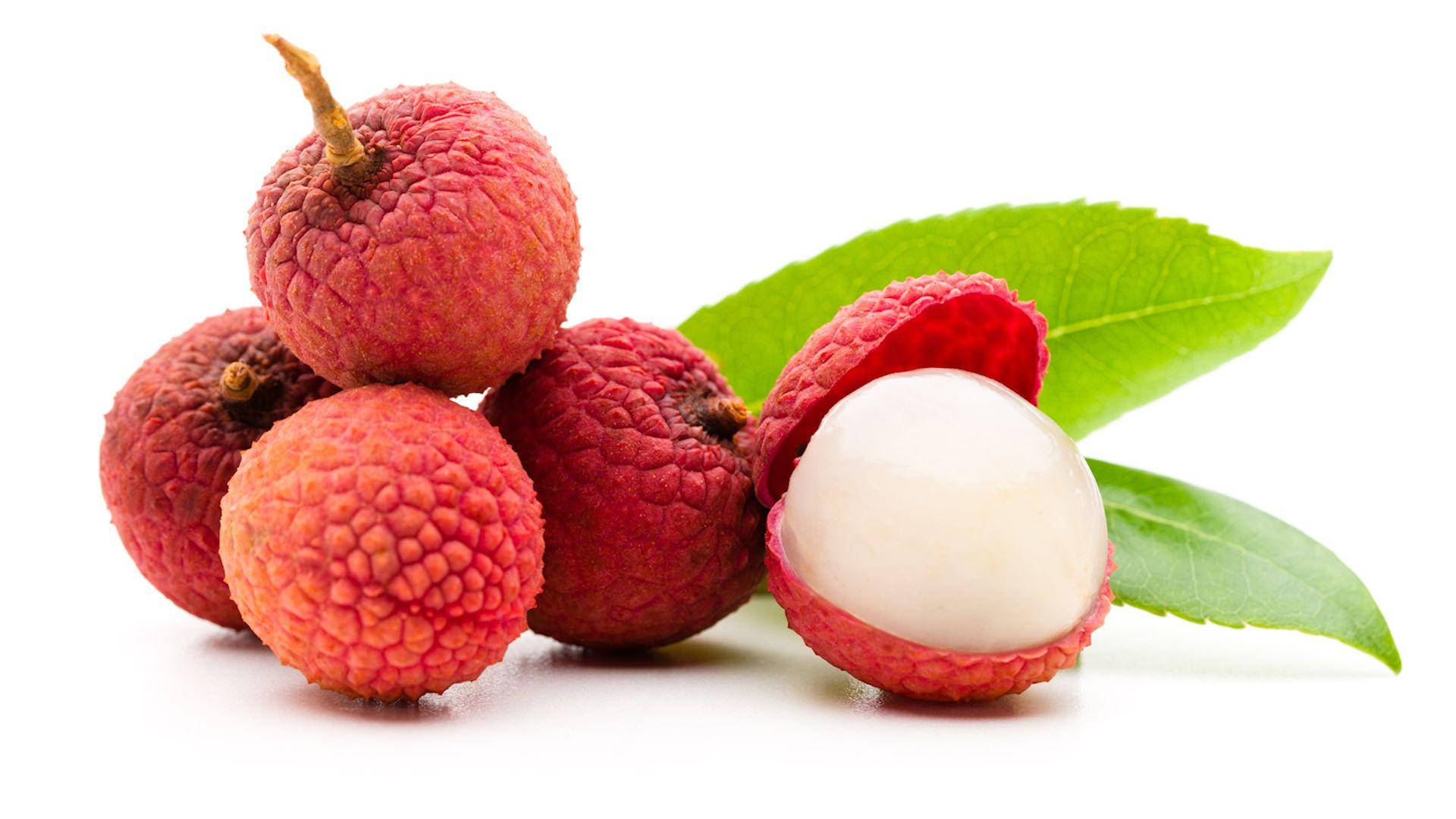 Fruits 桌布 壁紙 — 新鮮荔枝，帶有紋理的紅色外皮，其中一顆剝開，露出半透明的白色果肉，旁邊有綠葉，背景為白色。