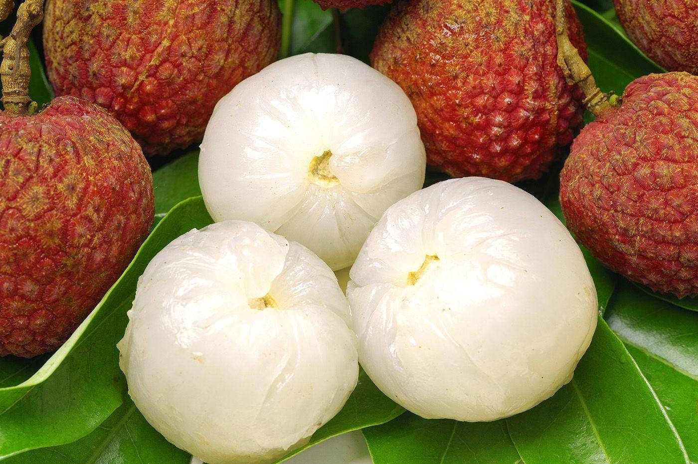 Fruits 桌布 壁紙 — 新鮮荔枝，帶紅色凹凸外皮和剝皮後的白色半透明果肉，放在鮮綠色的葉子上。