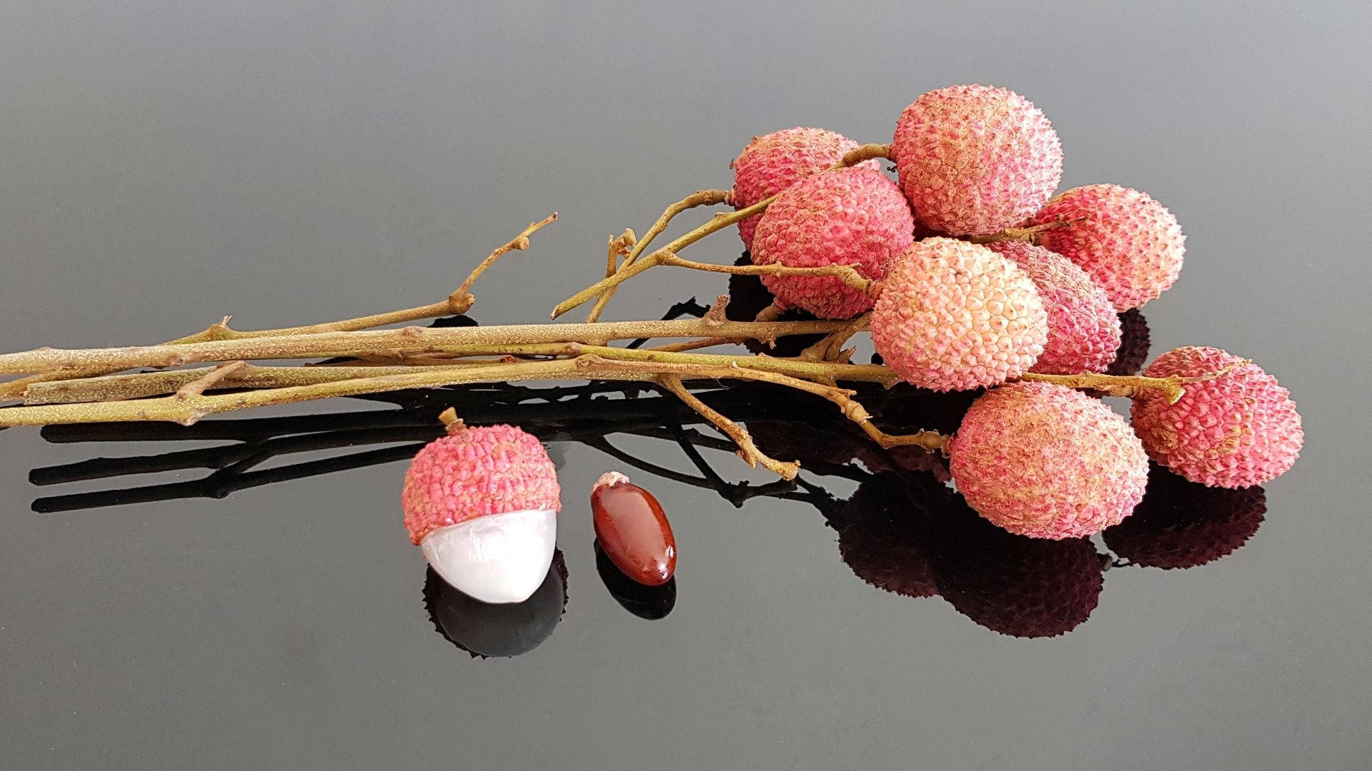 Fruits 桌布 壁紙 — 新鮮荔枝，粉紅色凹凸不平的外皮和白色果肉，放在深色反光表面上，旁邊有一粒籽。