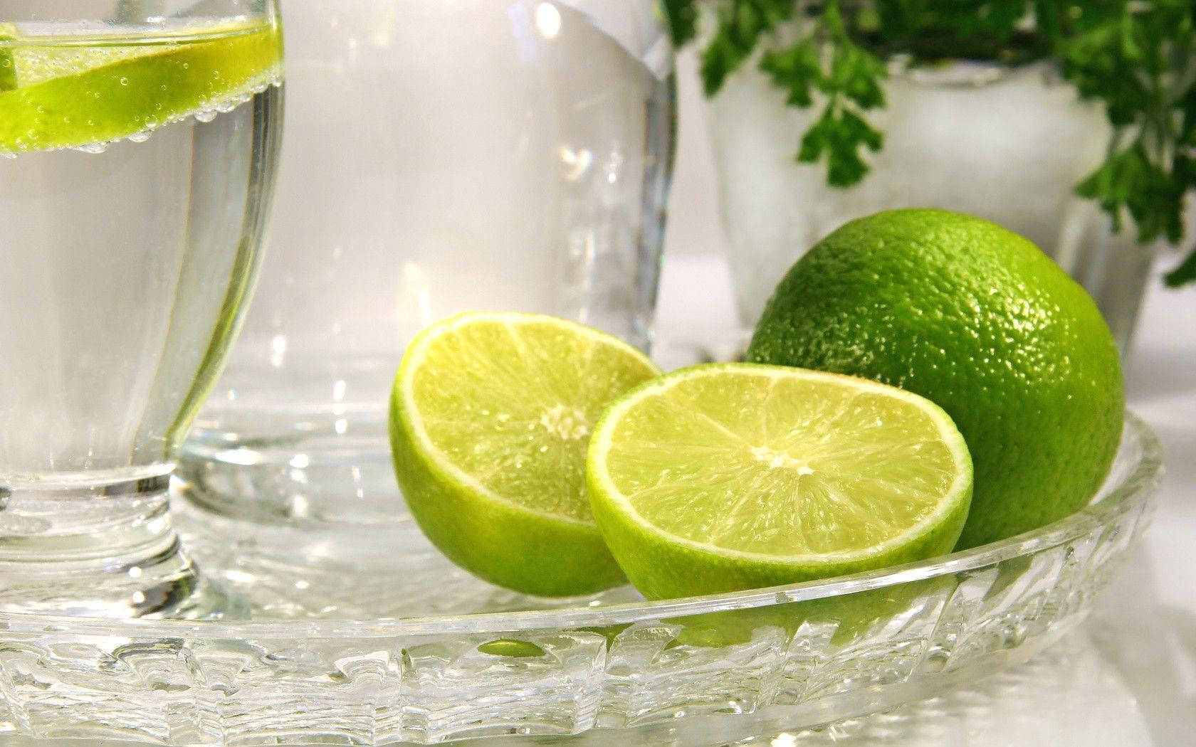 Drink 桌布 壁紙 — 新鮮萊姆片和整顆萊姆放在水晶托盤上，旁邊有一杯帶萊姆角的氣泡水。
