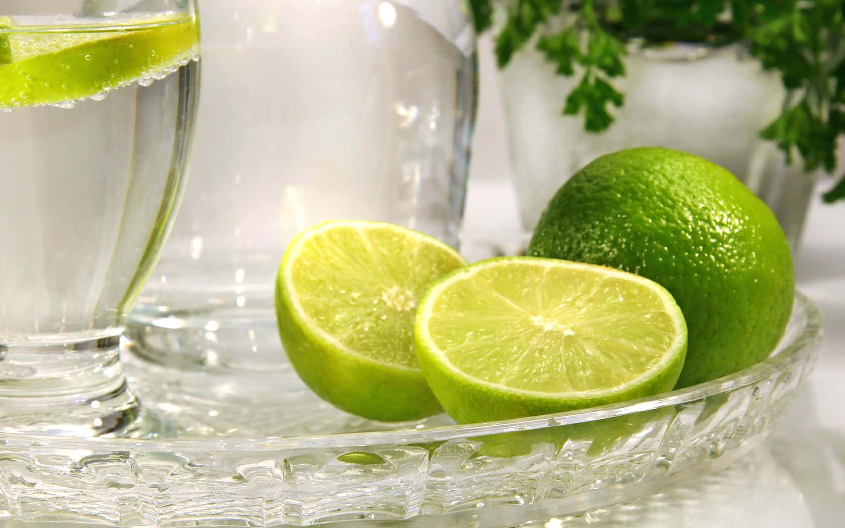 Lime 桌布 壁紙 — 新鮮萊姆片和整顆萊姆放在水晶托盤上，旁邊有一杯加了萊姆角的水。