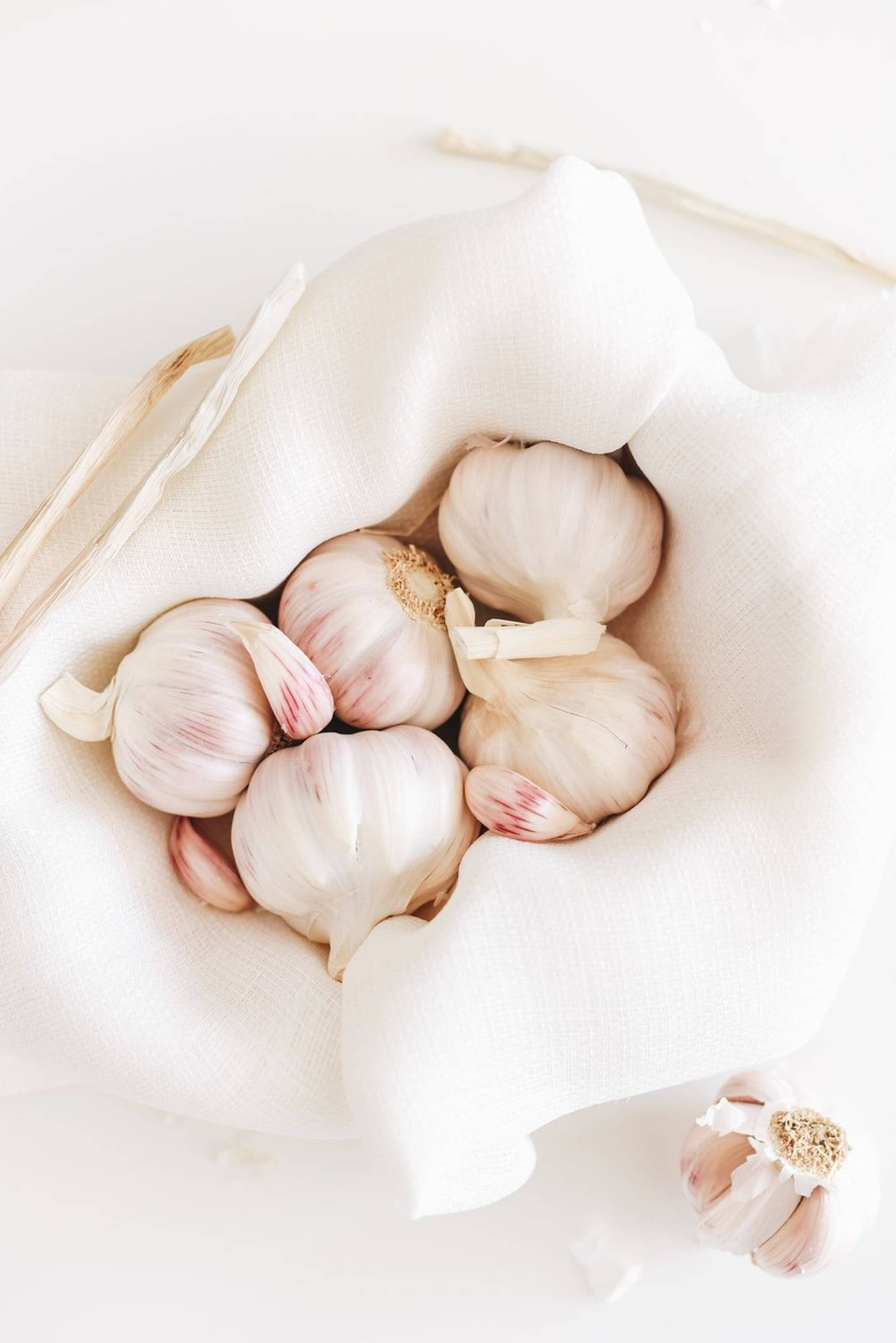 Garlic 桌布 壁紙 — 新鮮蒜頭包裹在柔軟白色布料中，襯以明亮簡約背景。