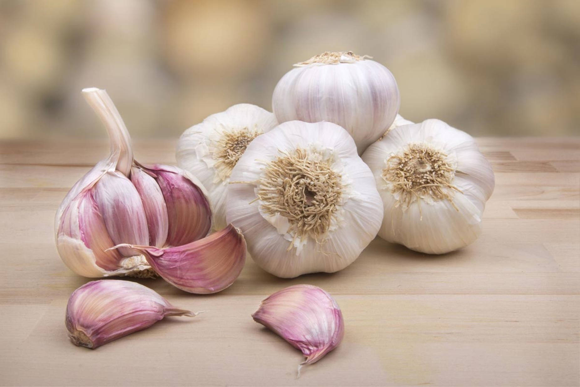 Garlic 桌布 壁紙 — 新鮮蒜頭和蒜瓣排列在淺色木質表面上，背景柔和模糊。