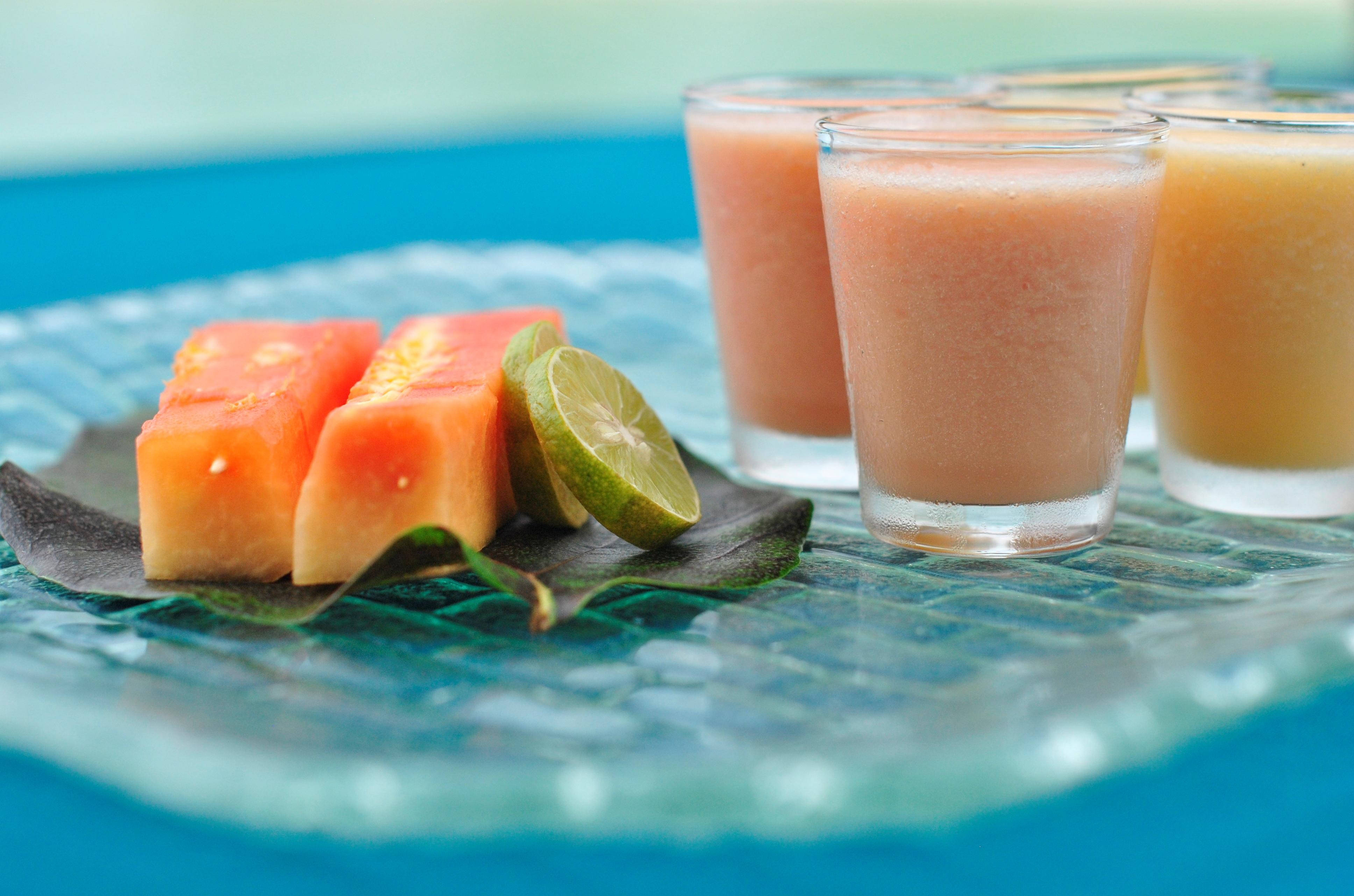 Smoothie 桌布 壁紙 — 新鮮製作的木瓜青檸冰沙，盛在玻璃杯中，搭配熱帶水果片，置於有紋理的藍色盤子上。