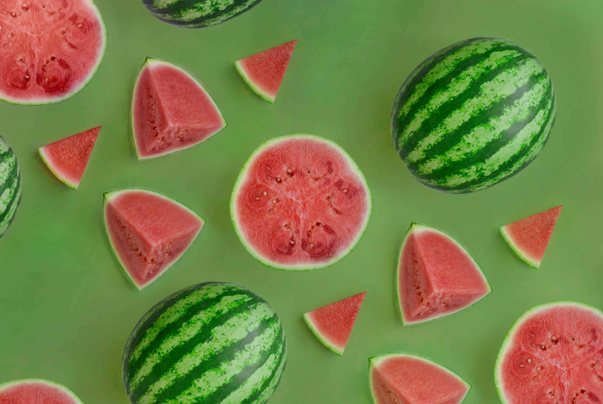 Watermelon 桌布 壁紙 — 新鮮西瓜切片和完整西瓜排列在充滿活力的綠色背景上，形成平鋪構圖。
