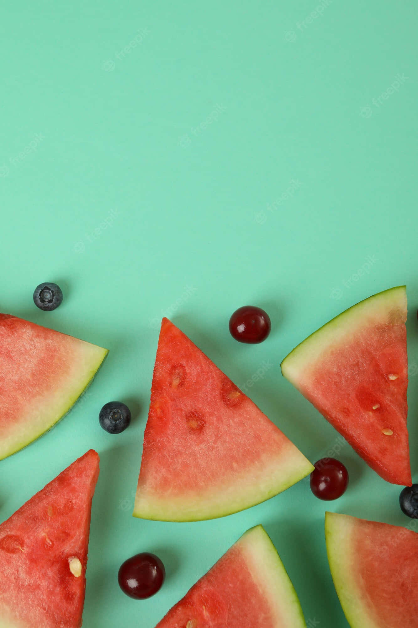 Watermelon iPhone 桌布 壁紙 — 新鮮西瓜片和莓果散落在薄荷綠色背景上的平鋪構圖。
