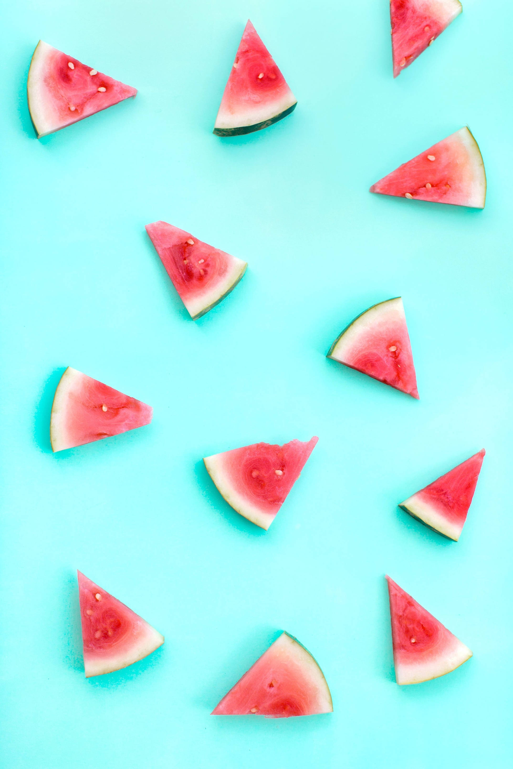 Watermelon 桌布 壁紙 — 新鮮西瓜片散落在充滿活力的藍綠色背景上，以平鋪構圖呈現。