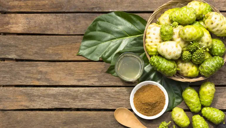 Fruits 桌布 壁紙 — 新鮮諾麗果和粉末擺放在質樸木板上，搭配大片葉子和一杯果汁。