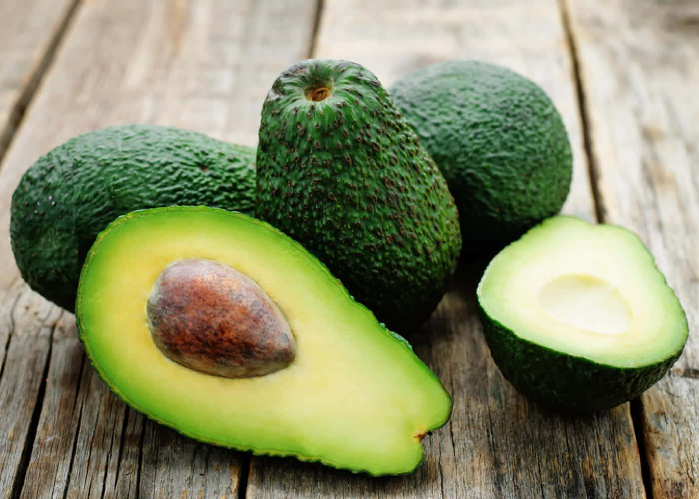 Avocado 桌布 壁紙 — 新鮮酪梨，其中一個切開一半，露出 creamy 果肉和果核，放在風化木板上。