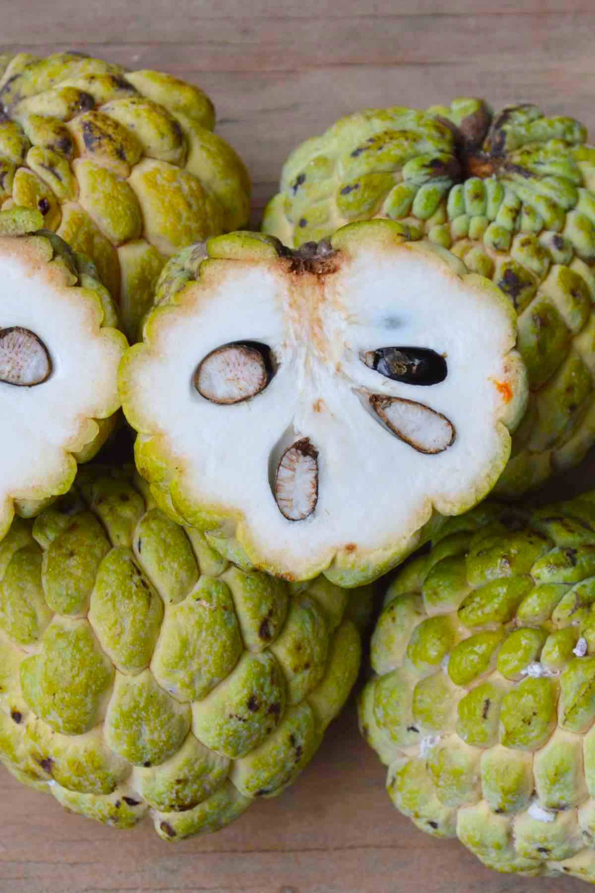 Fruit 桌布 壁紙 — 新鮮釋迦的近距離特寫，其中一個切開，露出奶油白色的果肉和黑色種子在木質表面上。