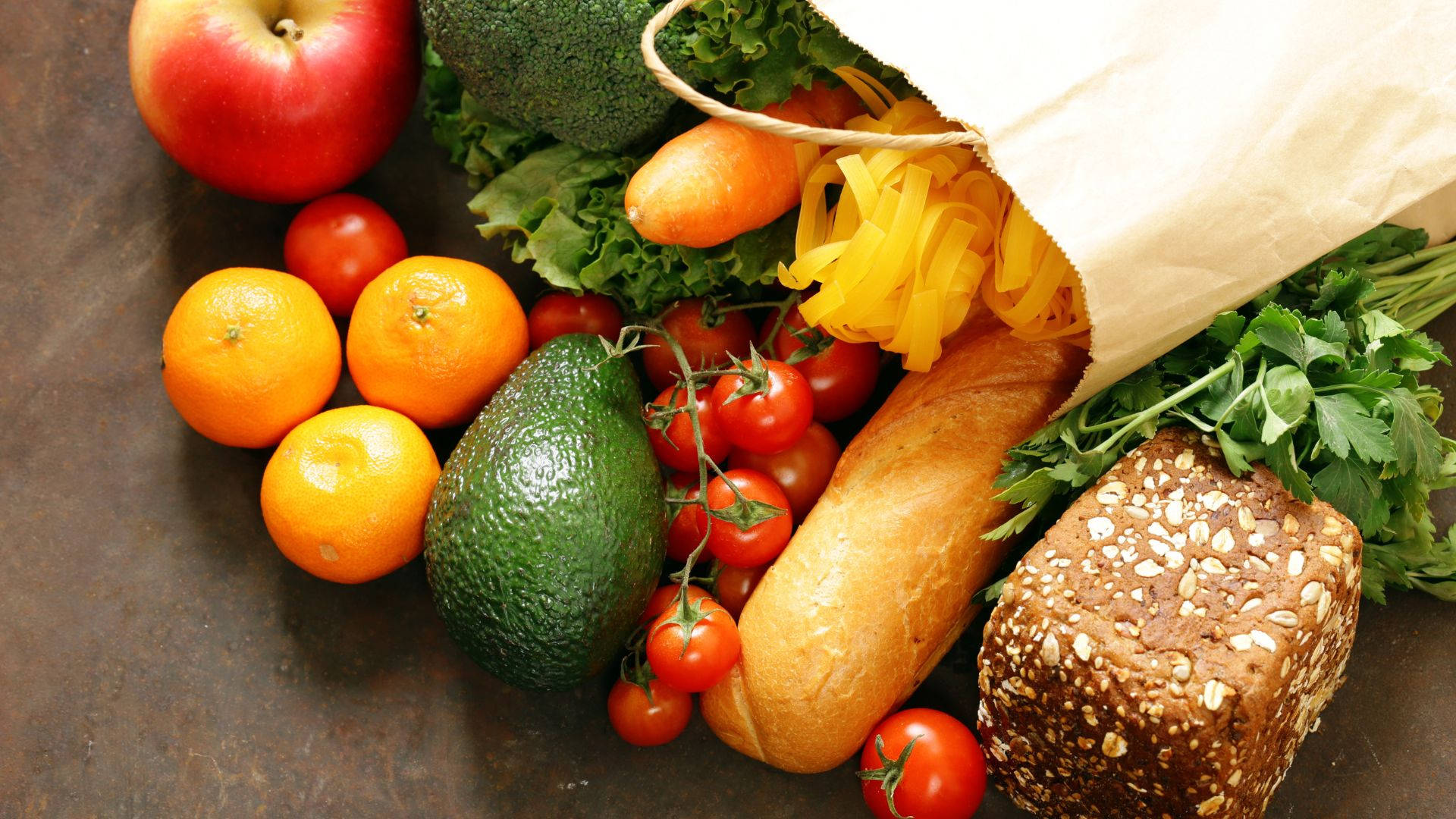 Fruits And Vegetables 桌布 壁紙 — 新鮮雜貨包括蘋果、柳橙、酪梨、櫻桃番茄、麵包和義大利麵從紙袋中溢出，落在鄉村風格的表面上。