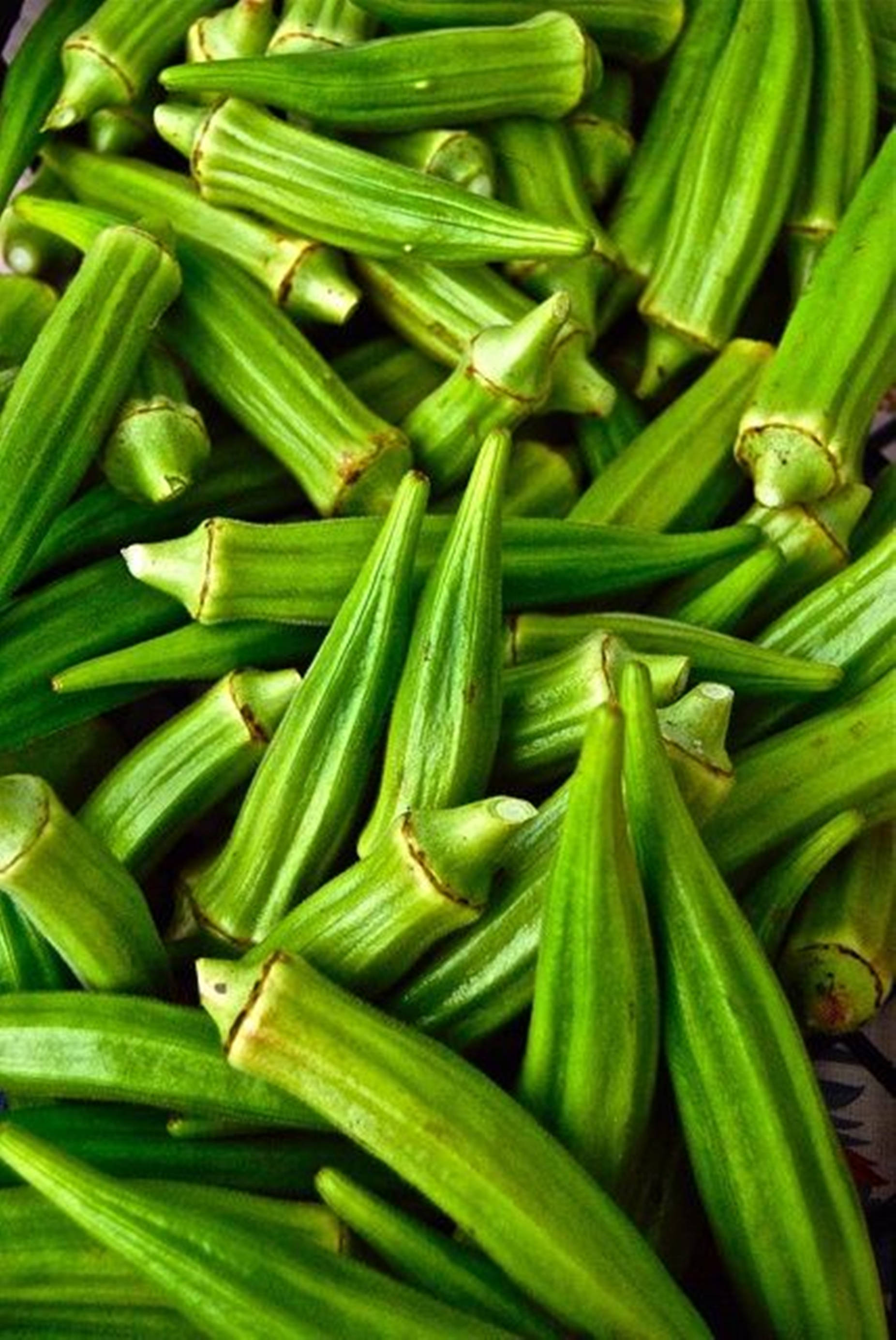 healthy 桌布 壁紙 — 新鮮青秋葵莢堆疊在一起的鮮明特寫，顯示其棱紋質感和尖頭。