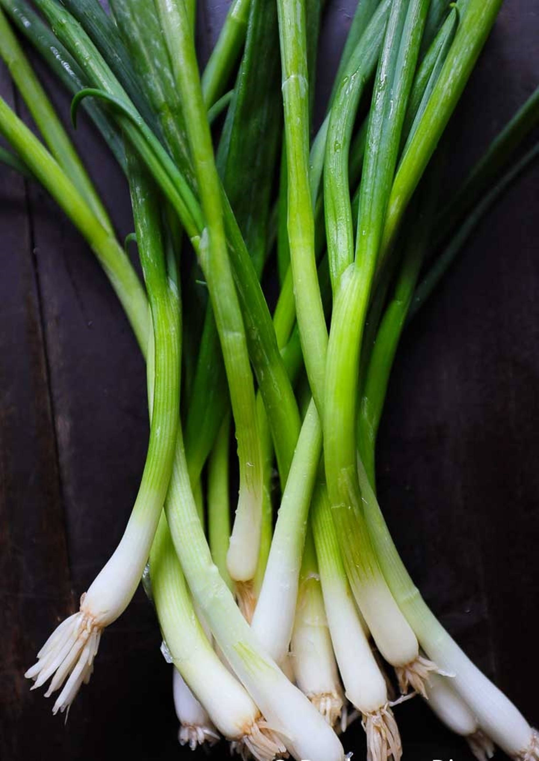 food iPhone 桌布 壁紙 — 新鮮青蔥，帶有爽脆的白色蔥頭和鮮綠色蔥葉，放在深色木質表面上。