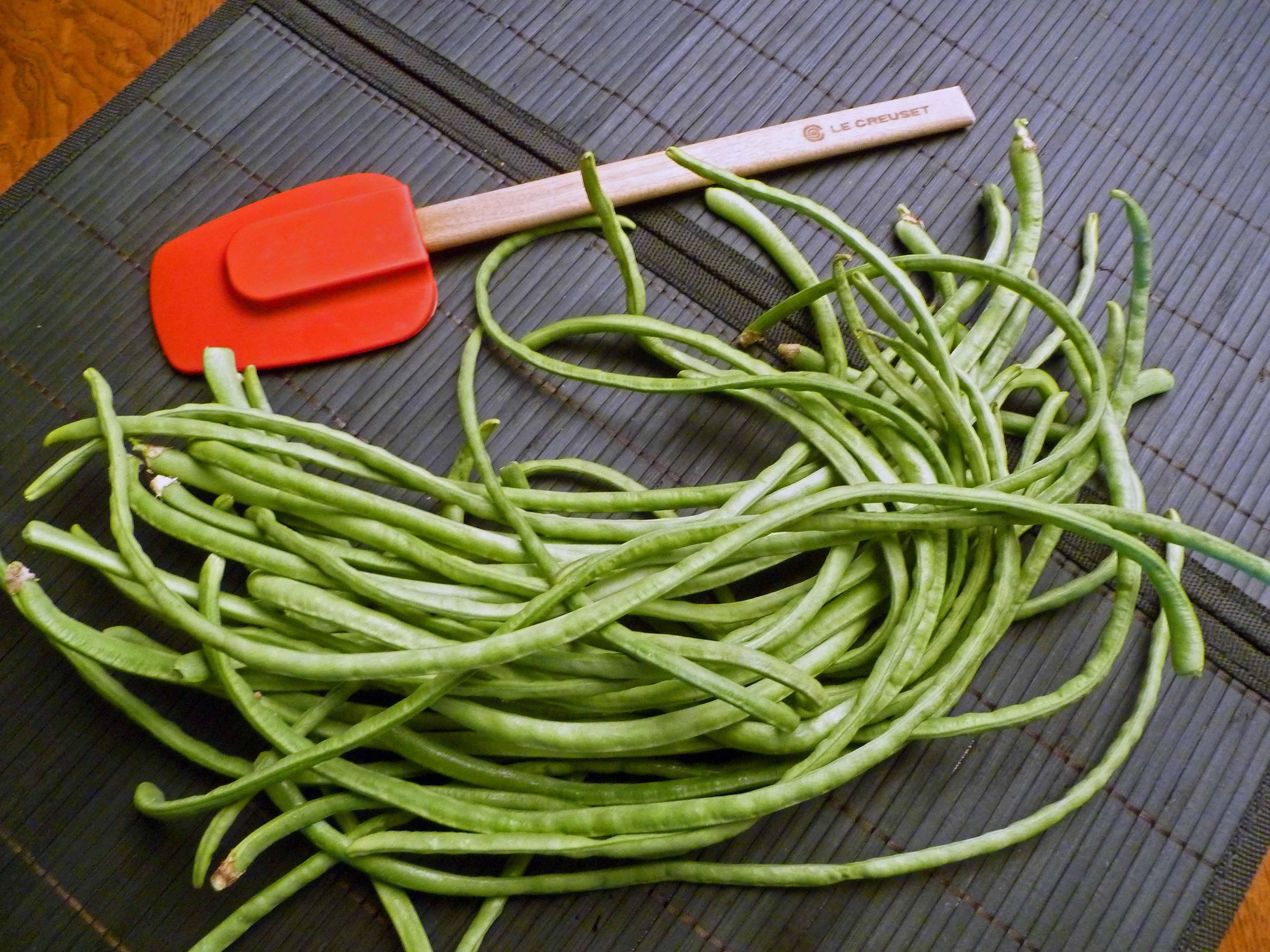 Long 桌布 壁紙 — 新鮮青豆堆在深色竹蓆上，旁邊有紅色矽膠鍋鏟。