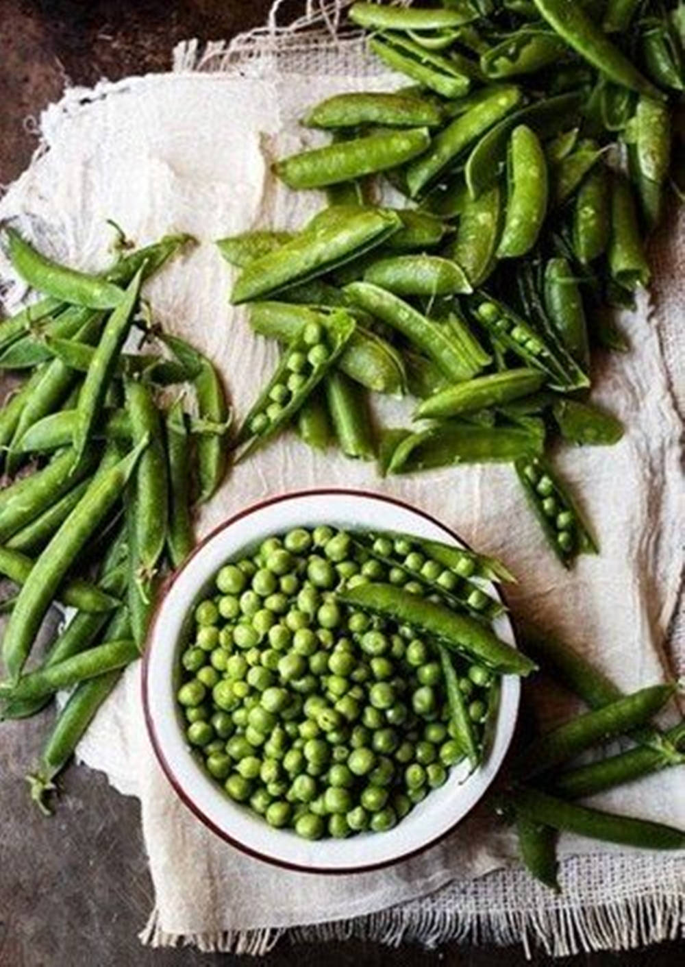beans 桌布 壁紙 — 新鮮青豆從打開的豆莢中溢出，落在質樸的布上，旁邊放著一碗充滿活力的圓形青豆。