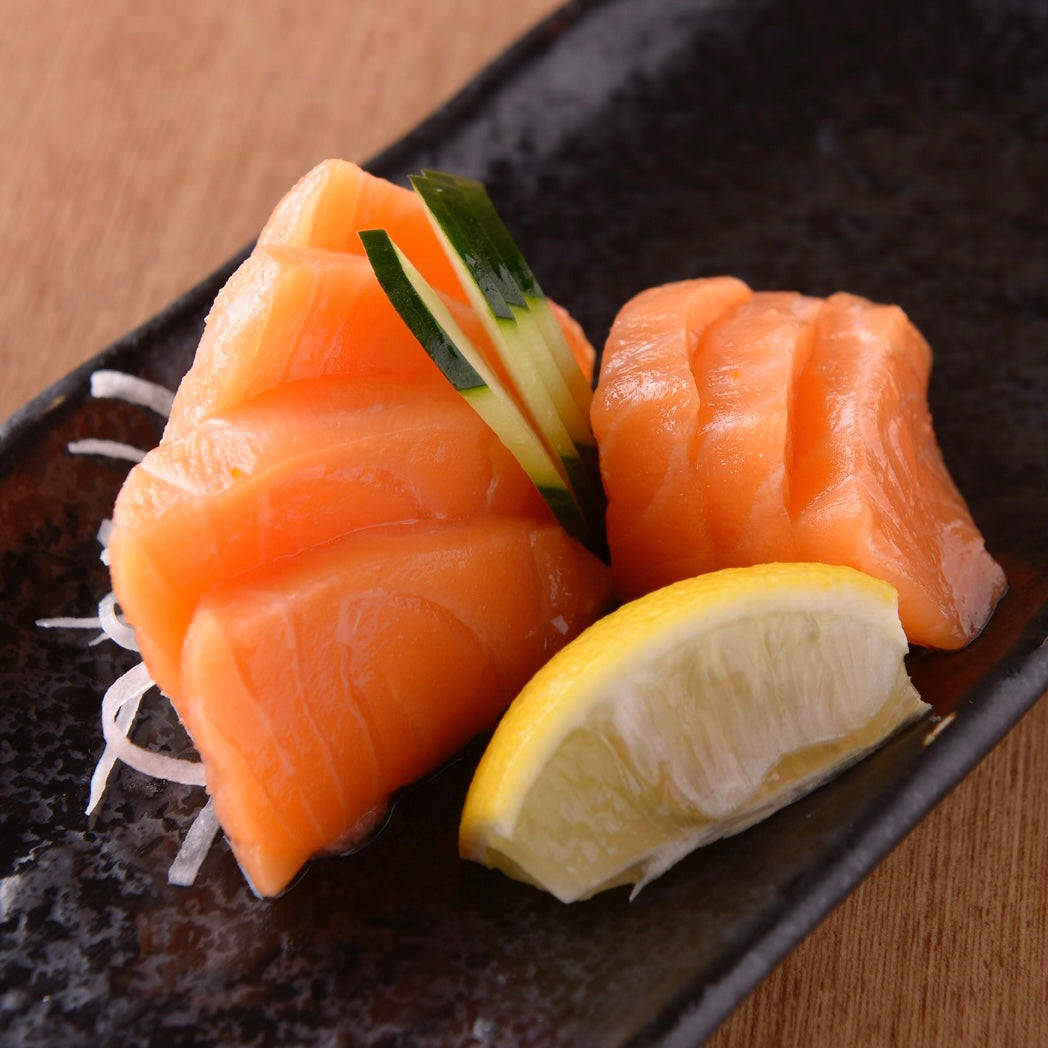Salmon 桌布 壁紙 — 新鮮鮭魚生魚片，搭配小黃瓜和檸檬角，放在深色陶瓷盤上。