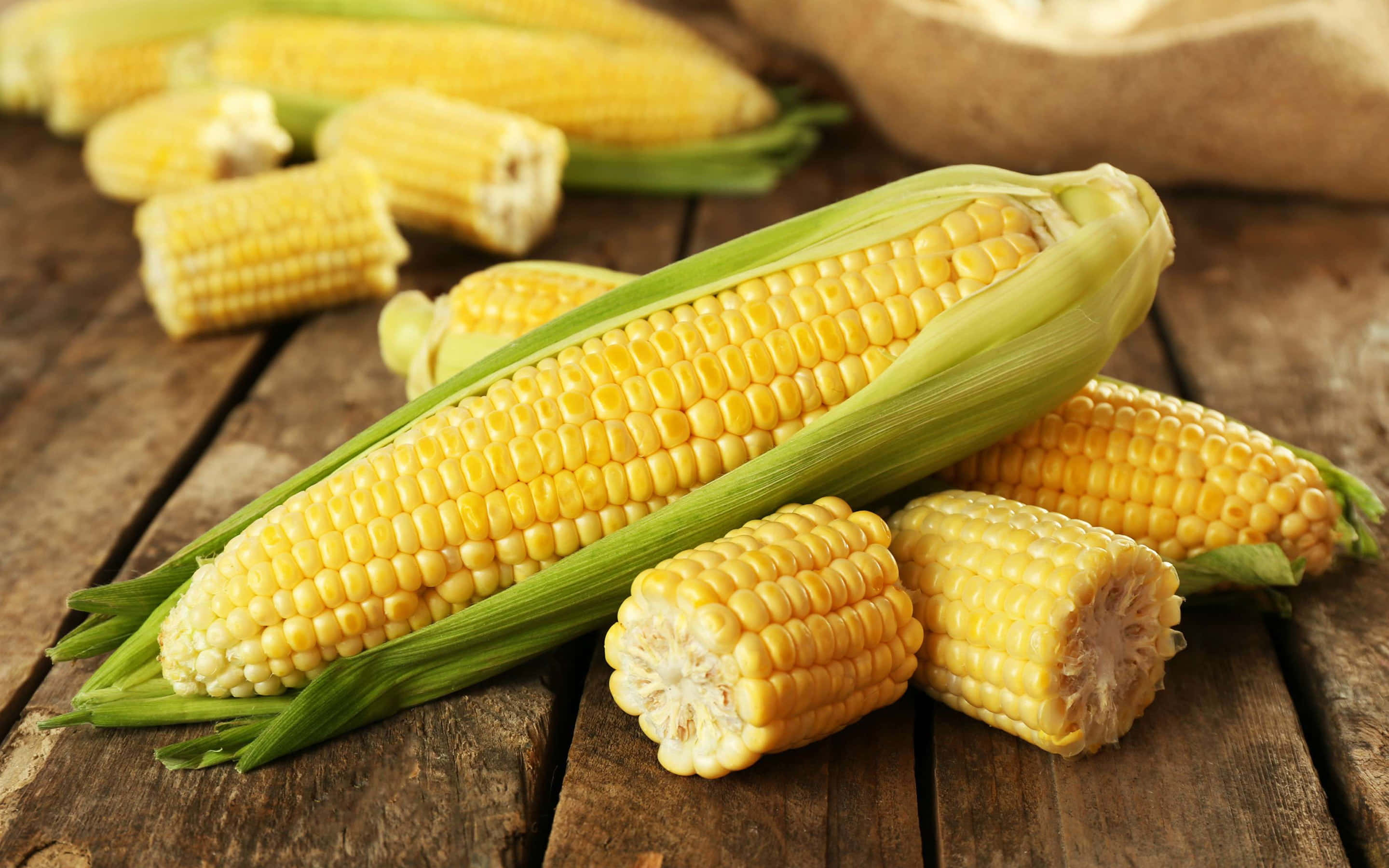 Yellow Corn 桌布 壁紙 — 新鮮黃色玉米連綠色外殼放在質樸的木桌上。