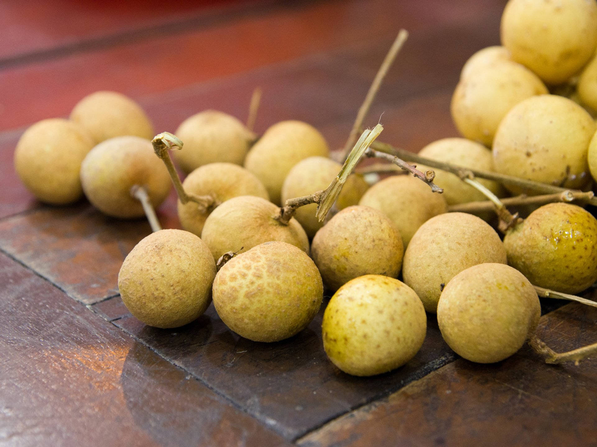Fruits 桌布 壁紙 — 新鮮龍眼果實，帶粗糙黃褐色外皮，置於深色木質表面上。