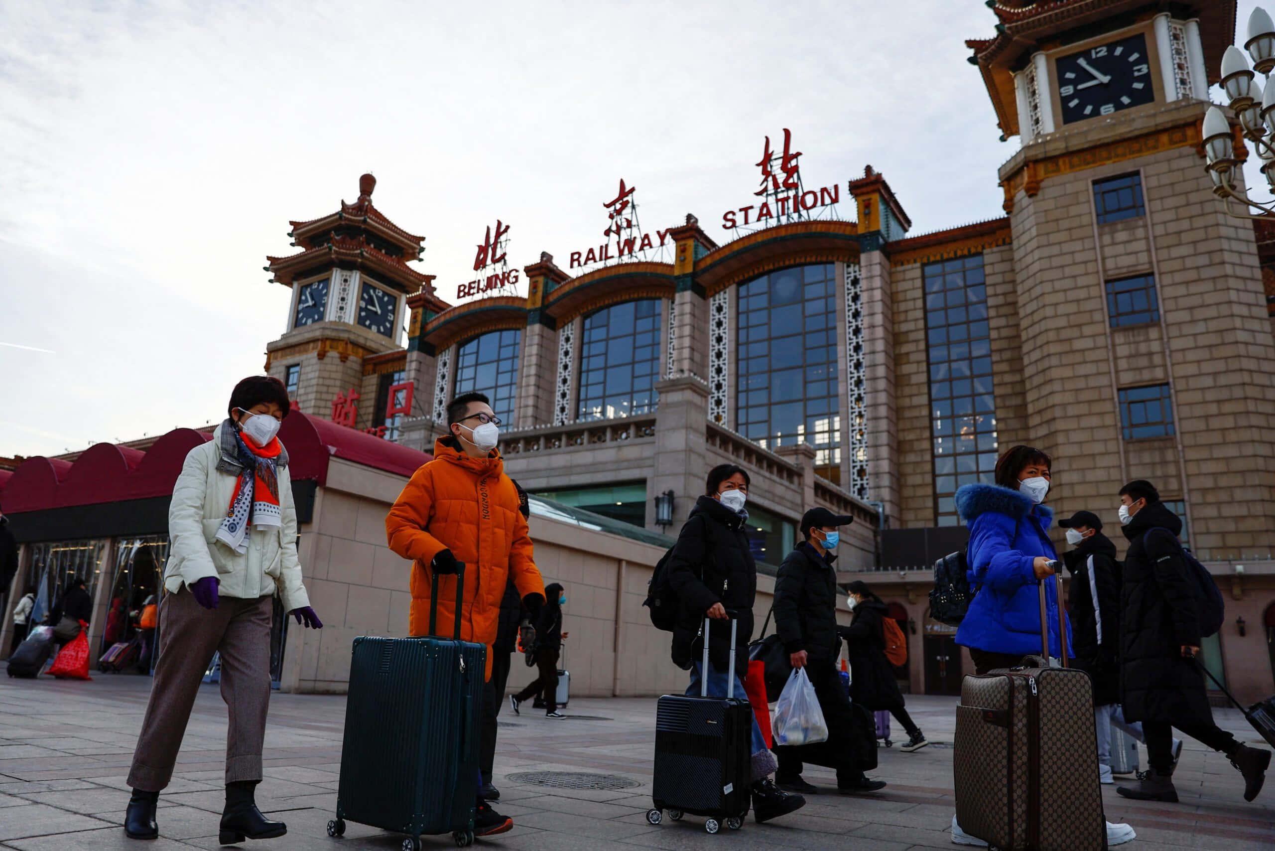 中文 桌布 壁紙 — 旅客拖著行李箱、戴著口罩，在陰天下的北京火車站外行走。