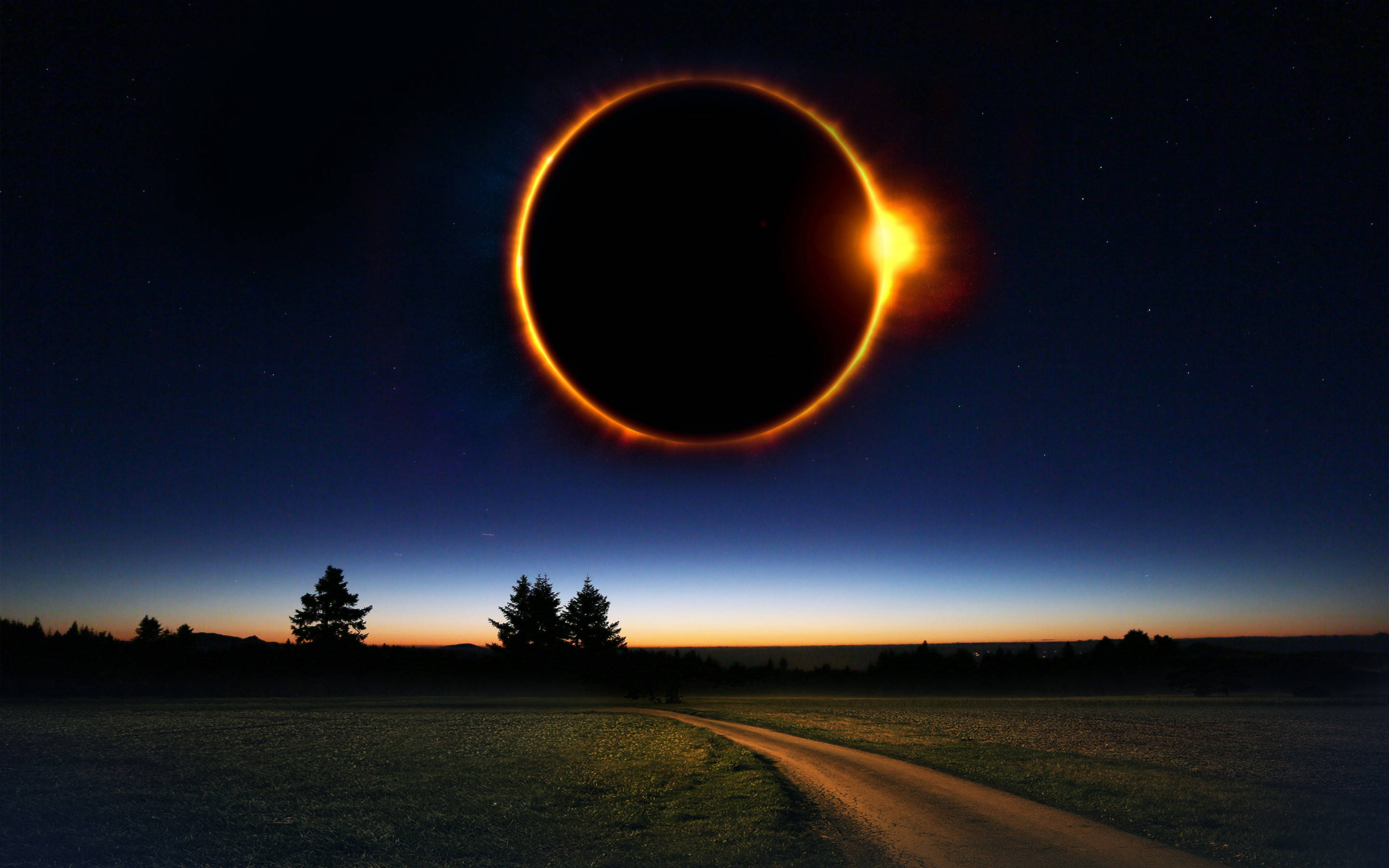 Eclipse 桌布 壁紙 — 日全食在暮色中將熾熱的日冕投射在寧靜的鄉村田野上，有一條蜿蜒的泥土小徑和剪影樹木。