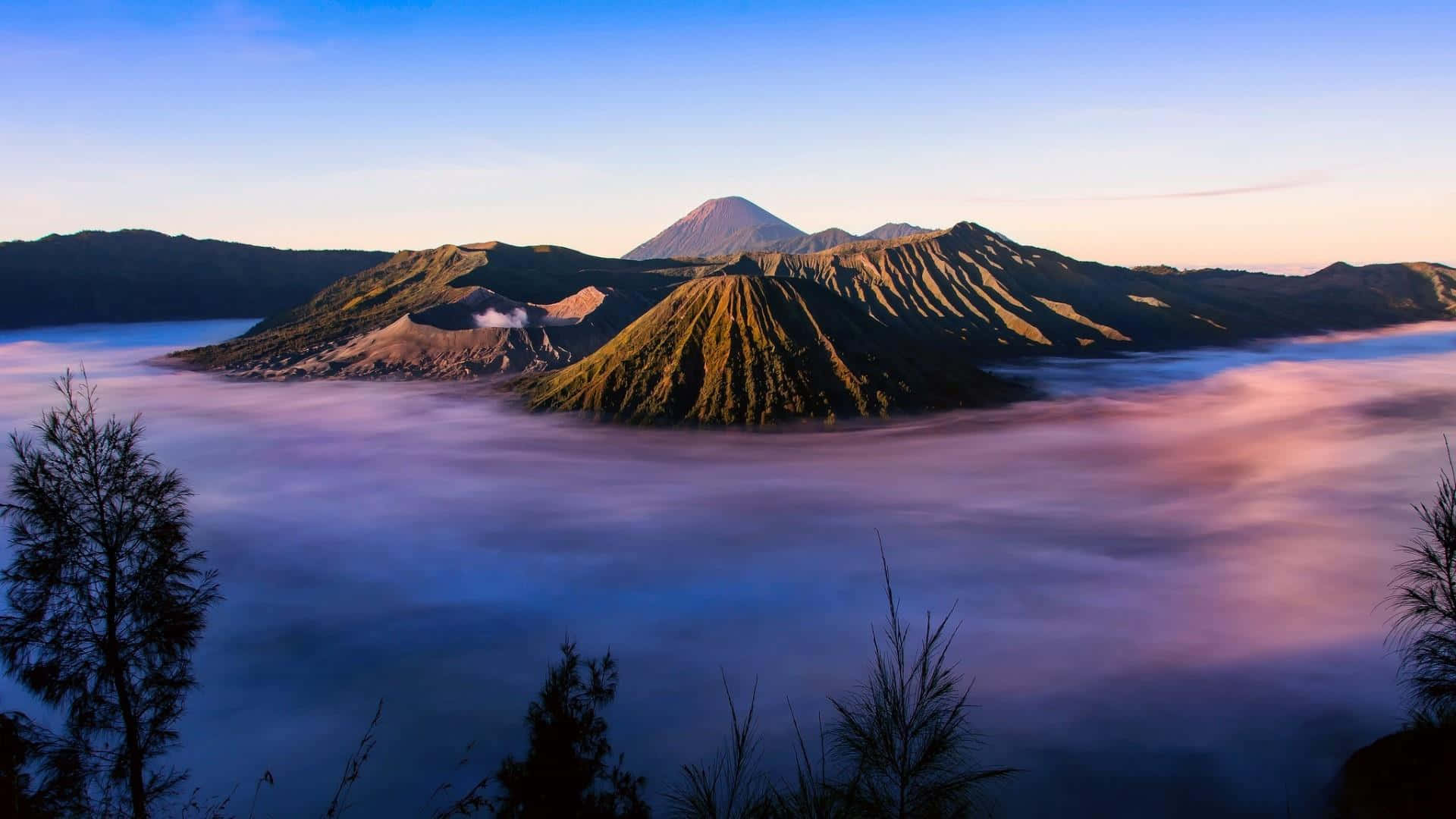 印尼 桌布 壁紙 — 日出以金色光芒沐浴火山峰，霧雲在下方旋轉，像一片紫色和藍色的海洋。