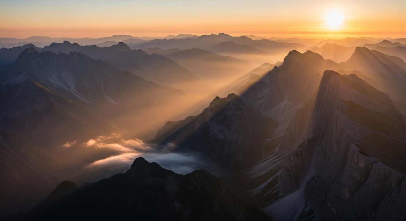 風景 桌布 壁紙 — 日出光芒穿透薄霧，照耀在層層疊疊的山峰上，將金色光輝灑落在崎嶇的地形上。