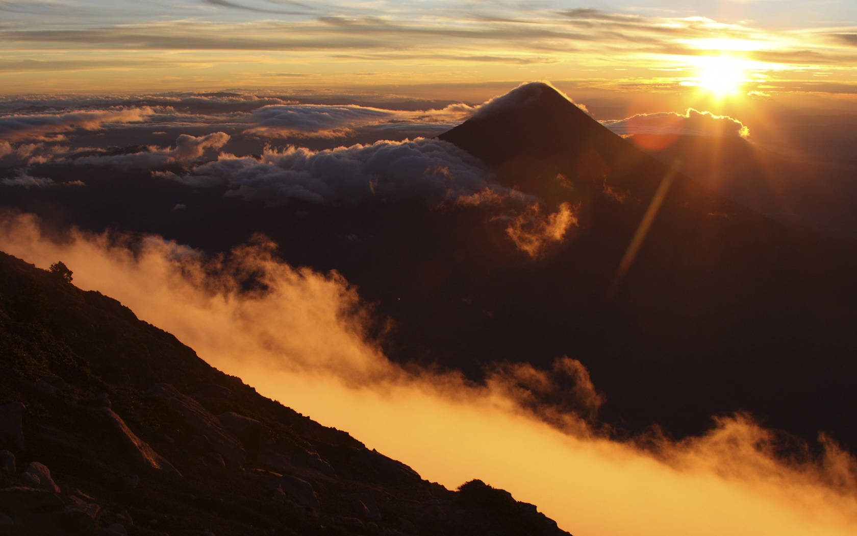 Guatemala 桌布 壁紙 — 日出在雲海之上，將金色光芒投射在山脊和下方霧氣瀰漫的山谷。