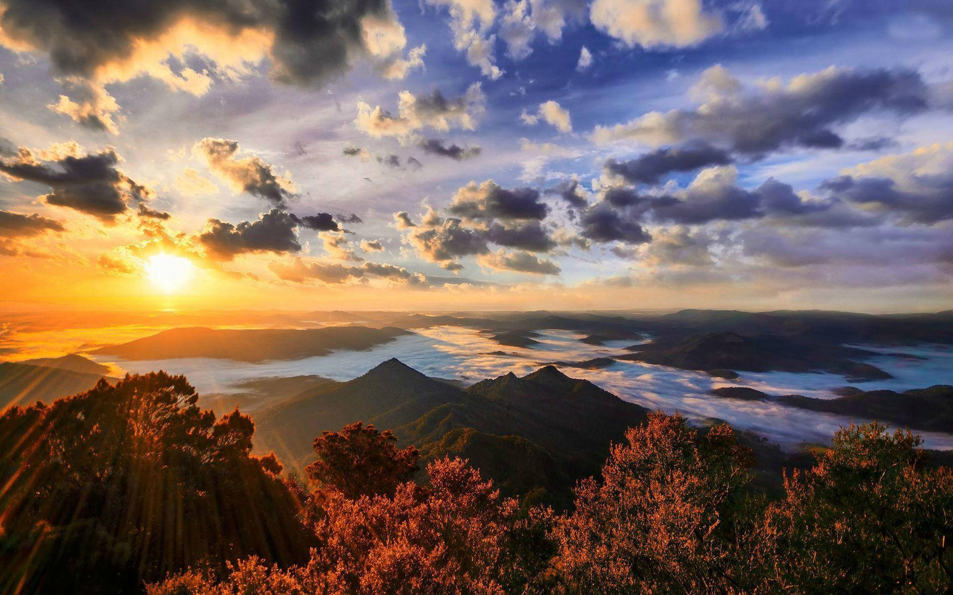 Smoky Mountains 桌布 壁紙 — 日出在霧氣瀰漫的山谷和森林覆蓋的山脊上，透過戲劇性的雲層繪出金色光芒。