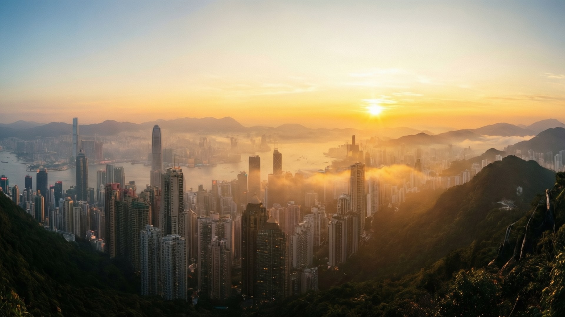 日出太平山頂 壁紙 — 日出將香港的天際線沐浴在金色光芒中，薄霧籠罩海港，摩天大樓從翠綠的山丘上拔地而起。