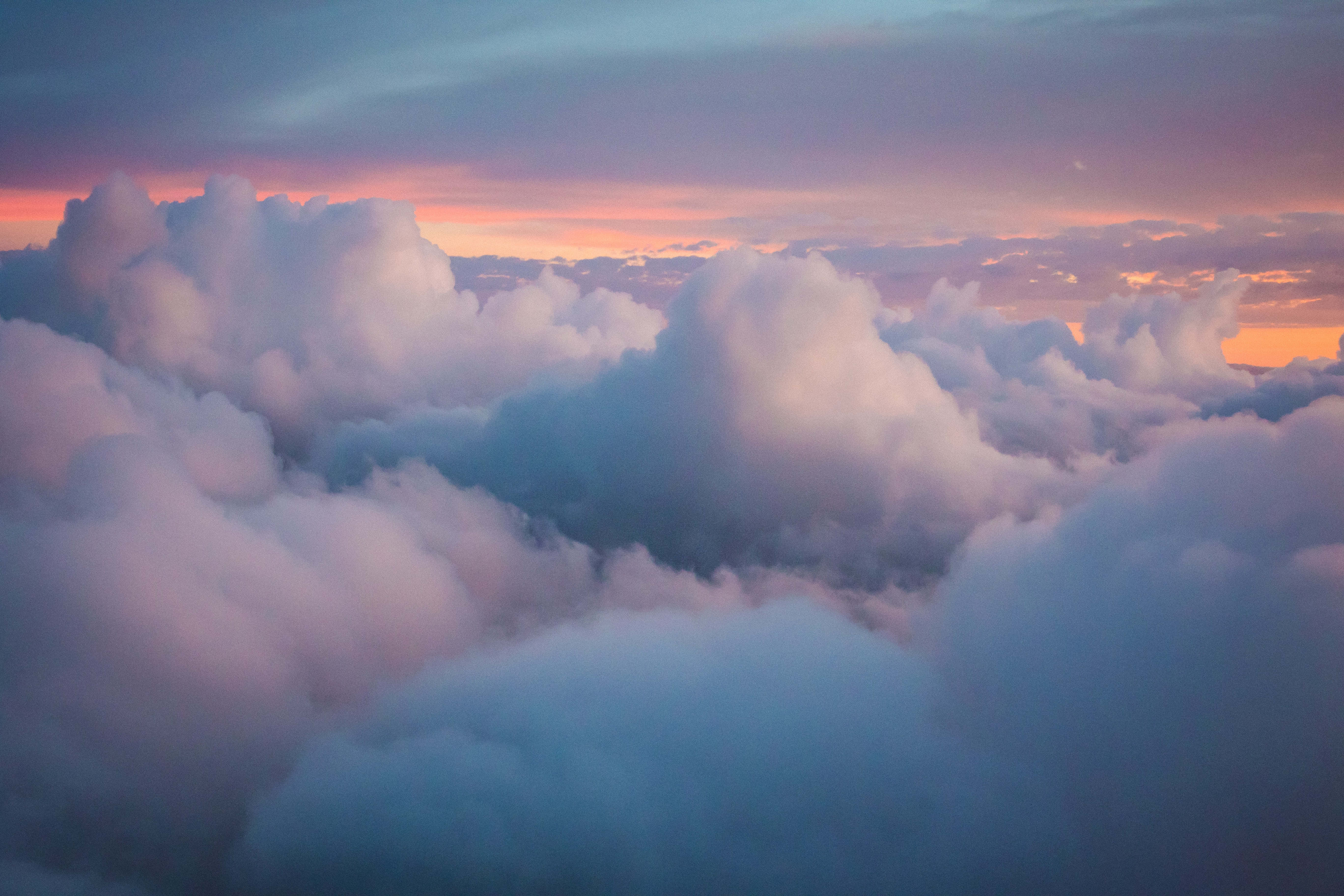 Clouds 4K 桌布 壁紙 — 日出時，蓬鬆的雲朵沐浴在柔和的粉紅色和藍色暮色中的鳥瞰圖。