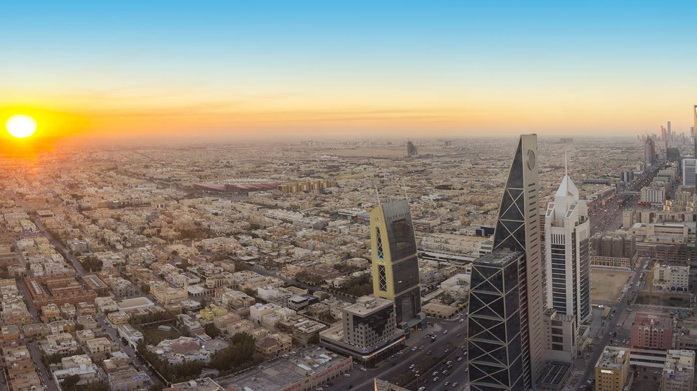 Riyadh 桌布 壁紙 — 日出時分，廣闊城市天際線的鳥瞰圖，金色陽光照射著現代摩天大樓和密集的城市網格。
