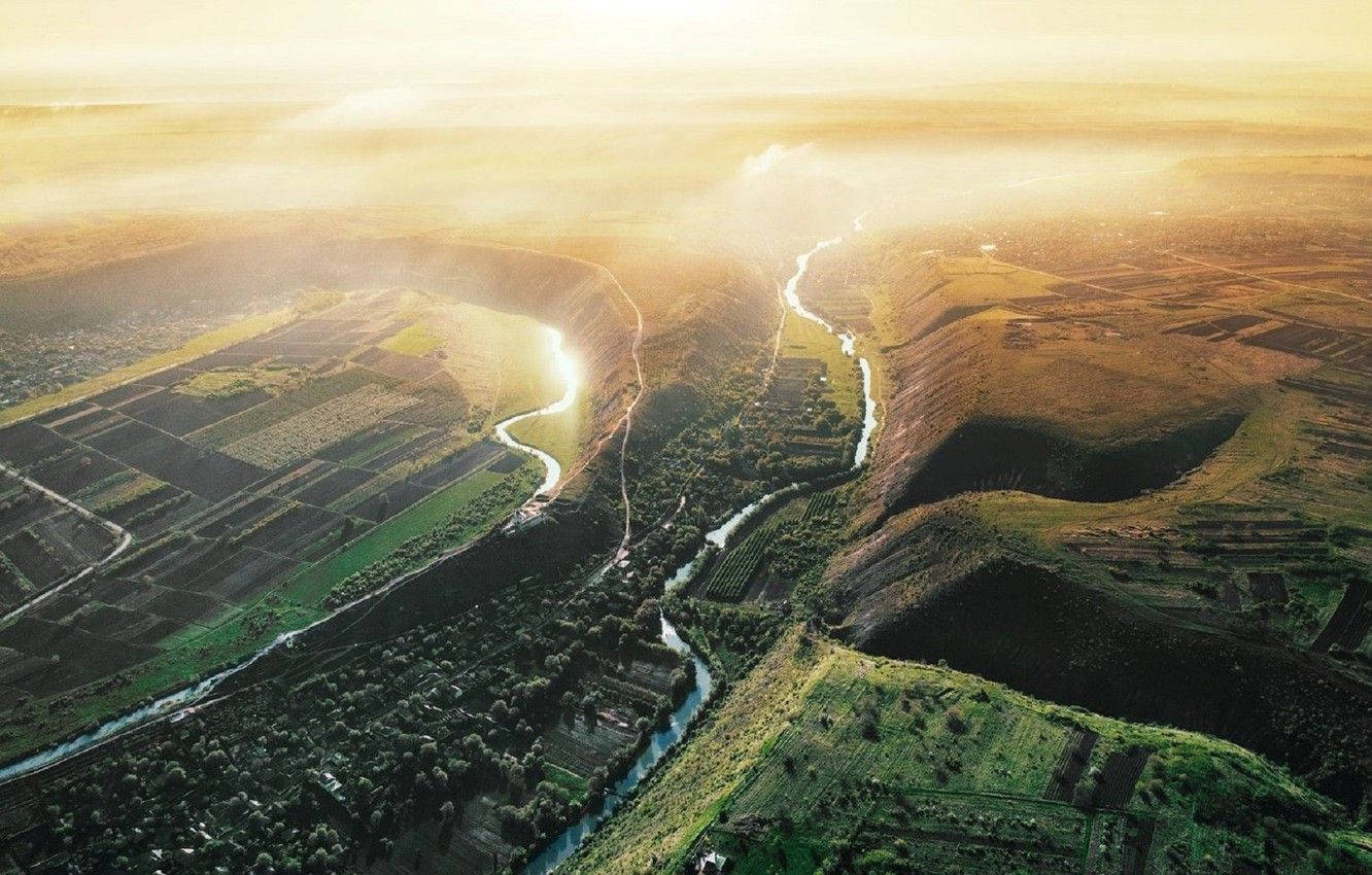 Moldova 桌布 壁紙 — 日出時分，蜿蜒的河流穿過金色田野和綠色山丘的鳥瞰圖，帶有霧氣瀰漫的氛圍。