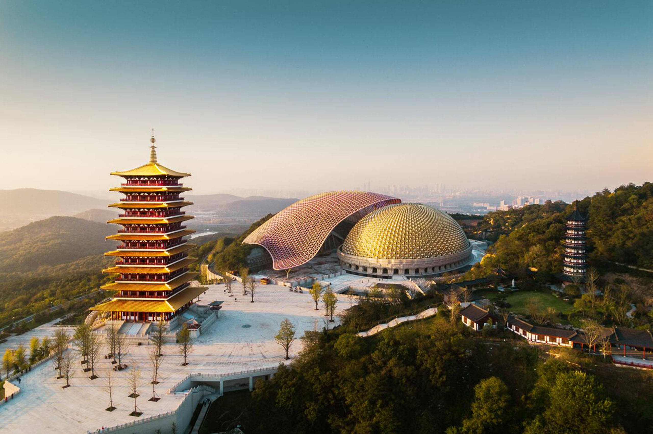 Nanjing 桌布 壁紙 — 日出時分，金色寶塔和圓頂寺廟建築群坐落在翠綠山丘之間的鳥瞰圖。