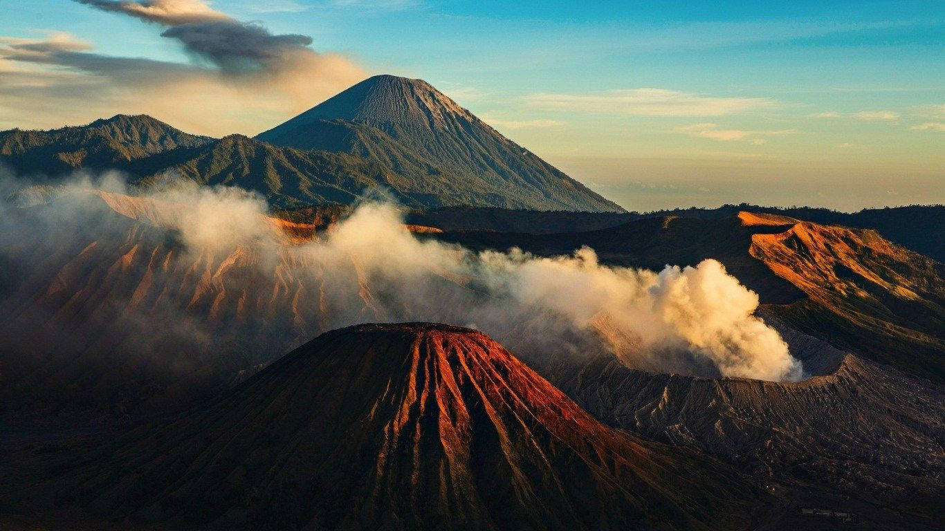 筆電 桌布 壁紙 — 日出時分，雄偉的火山景觀，火山口升起蒸氣，崎嶇的山峰沐浴在金色光芒中。