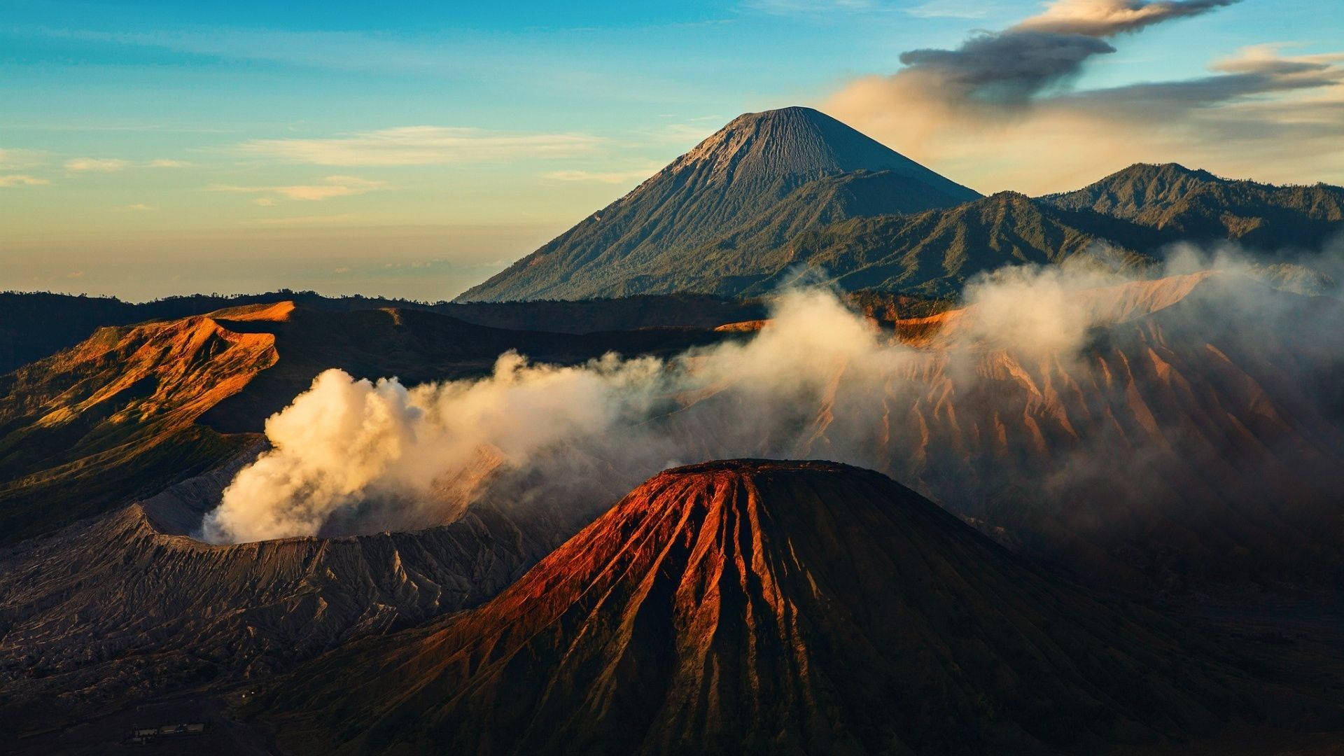 Mac 桌布 壁紙 — 日出時分，雄偉的火山景觀，蒸氣從火山口升起，高聳的山峰沐浴在金色光芒中。