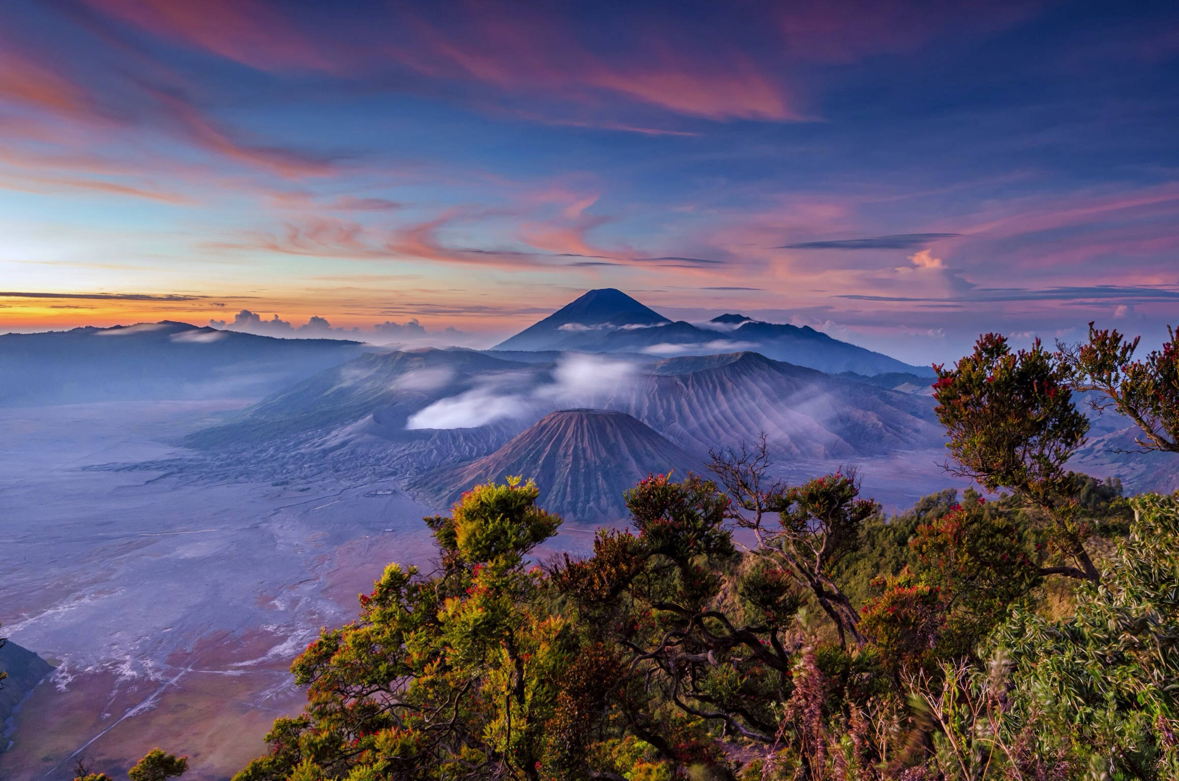 印尼 桌布 壁紙 — 日出時分的雄偉火山景觀，層巒疊嶂，霧氣瀰漫的山谷，以及充滿活力的紫橙色天空。