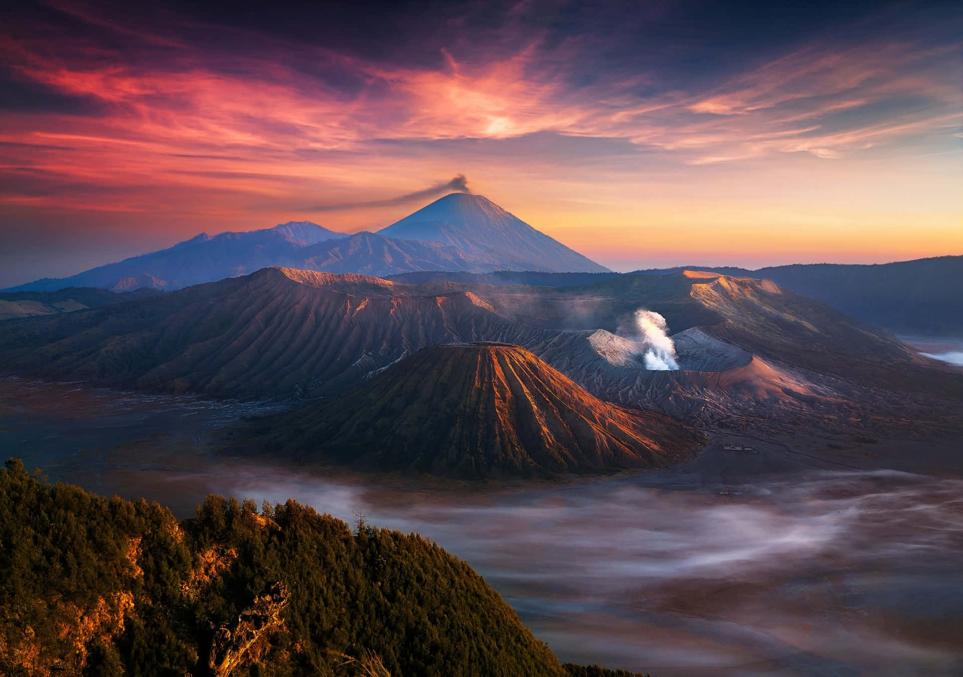 印尼 桌布 壁紙 — 日出時分的雄偉火山景觀，霧氣繚繞的山脈和冒著蒸汽的火山口上方，是充滿活力的粉紅色和橙色天空。