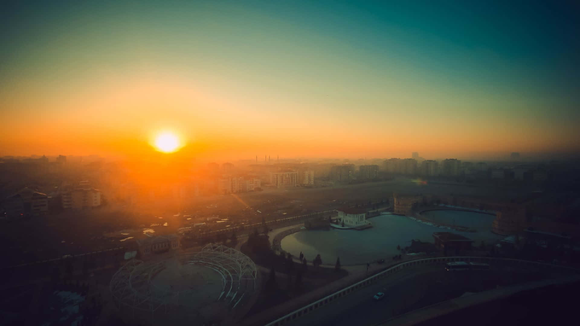 日出 桌布 壁紙 — 日出時城市景觀的鳥瞰圖，金色光線在建築物和中央廣場上投下長長的陰影。