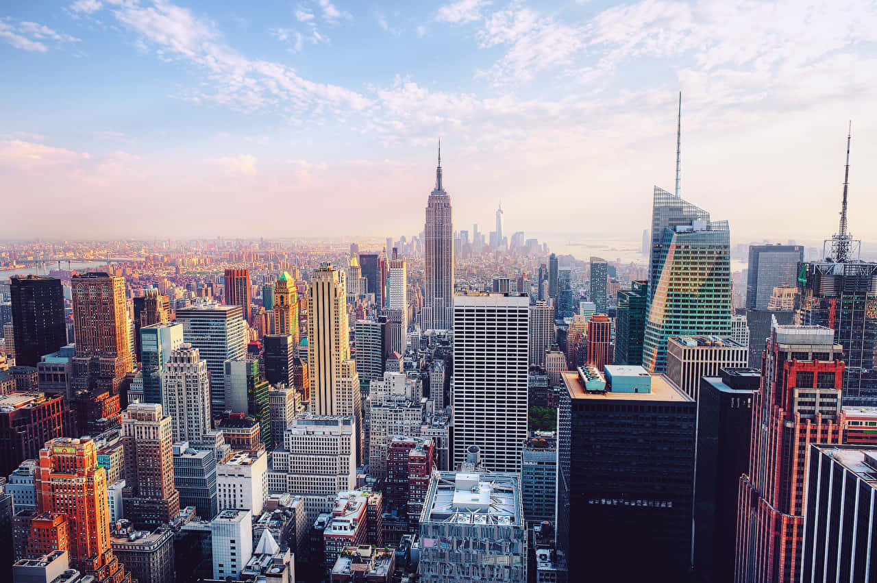 New York City 4K Ultra HD 桌布 壁紙 — 日出時紐約市天際線的空中景觀，金色光芒照亮摩天大樓和散落的雲層。