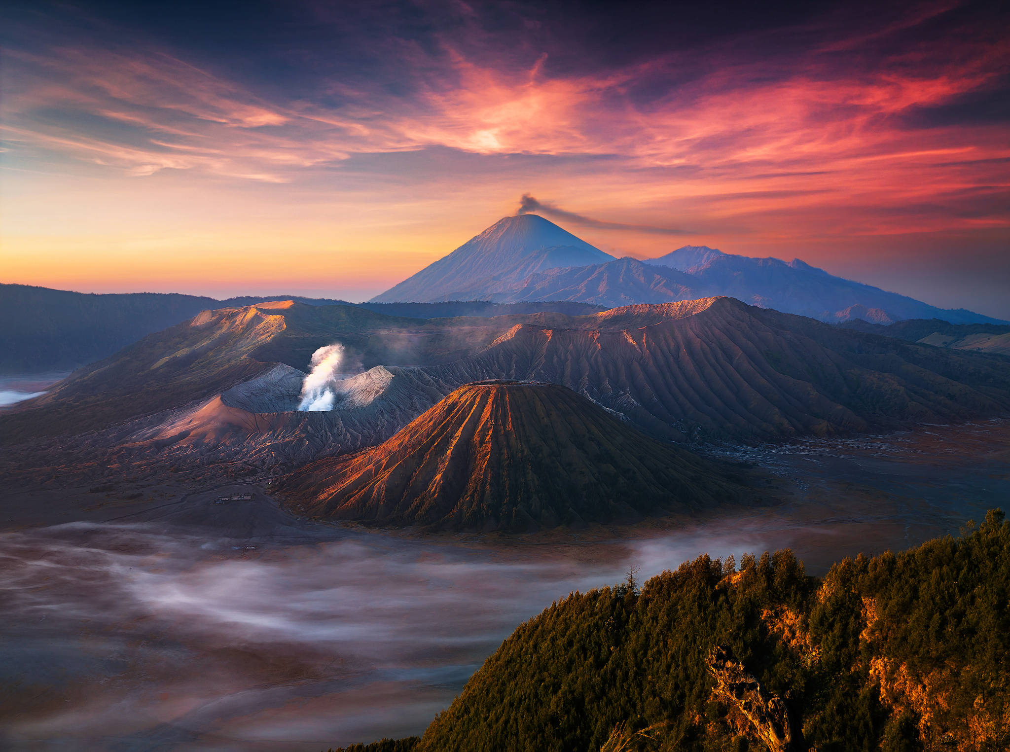 印尼 桌布 壁紙 — 日出時雄偉的火山景觀，崎嶇的山峰和霧氣繚繞的山谷上方有火紅的橙色和粉紅色雲彩。