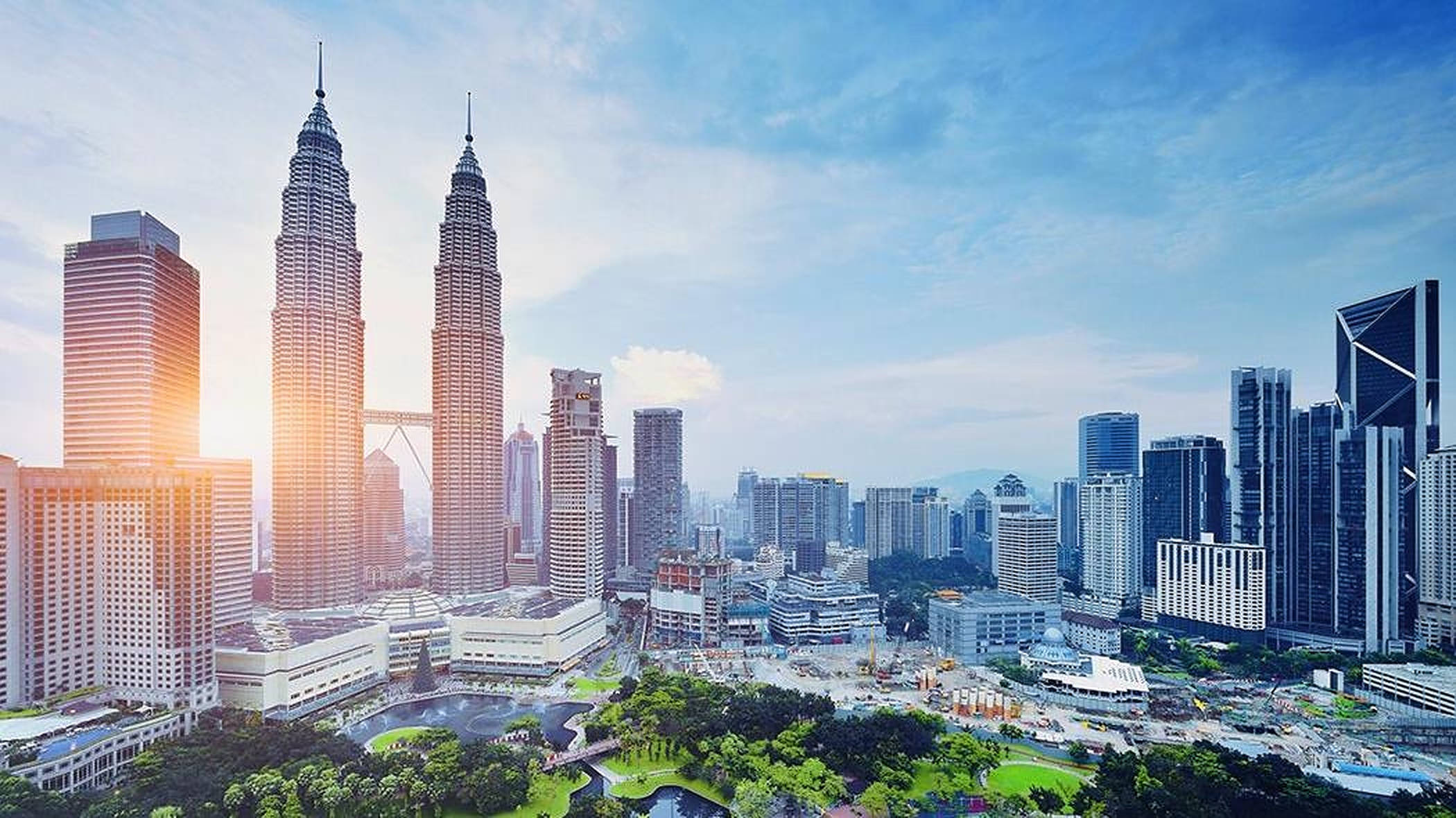Kuala 桌布 壁紙 — 日出照亮了標誌性的雙峰塔及周圍的摩天大樓，映襯著湛藍的天空和散落的雲朵。