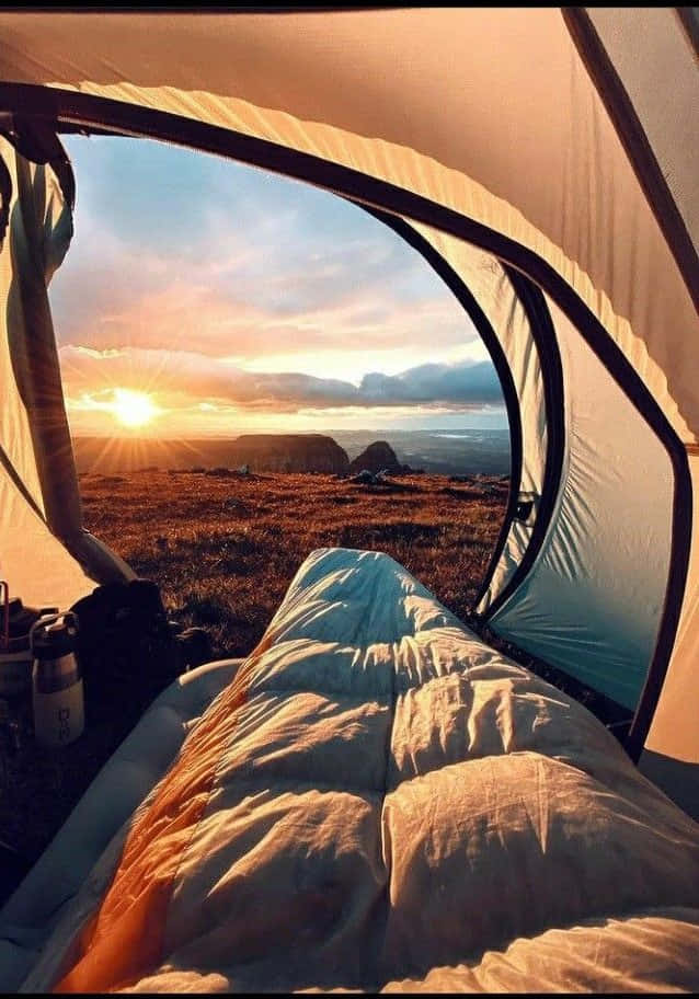 Minimalist Camping 桌布 壁紙 — 日出穿過帳篷開口閃耀，顯露出睡袋和崎嶇的山景。