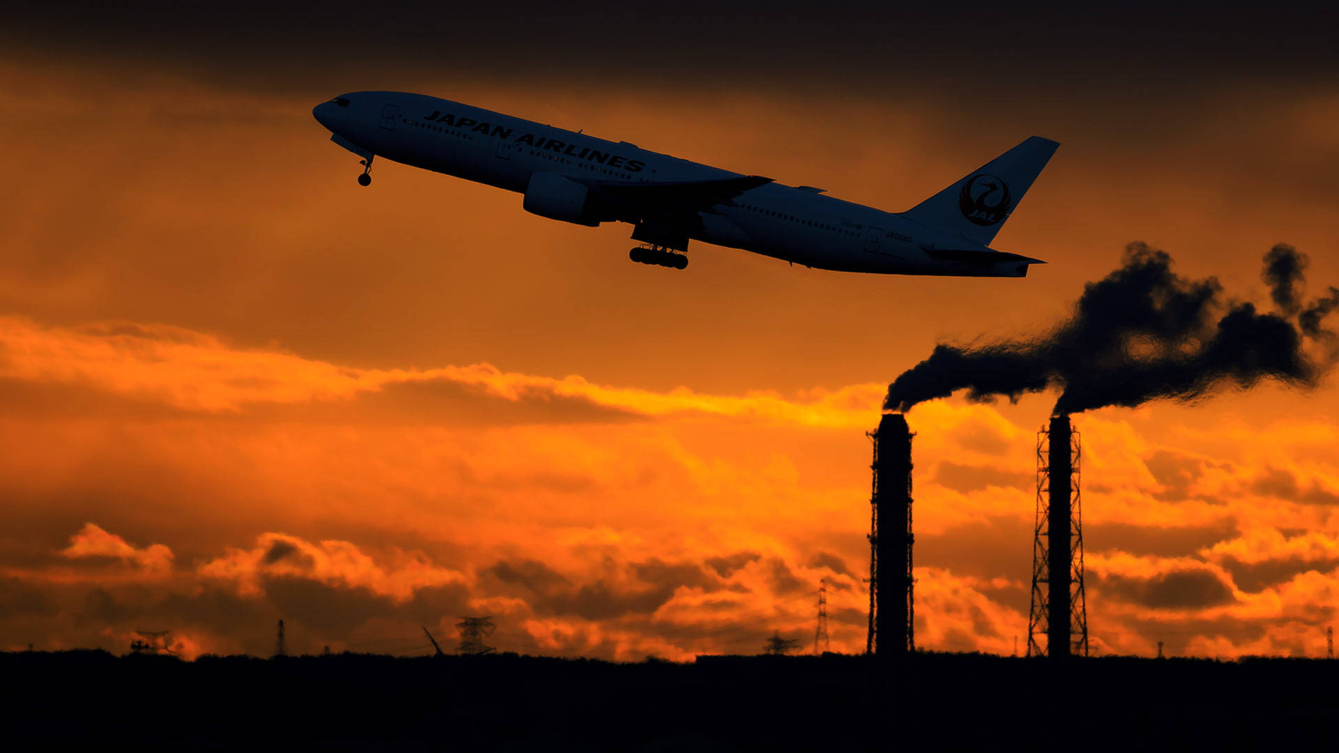 日本航空的飛機在日落時分飛越排放煙霧的工業煙囪。