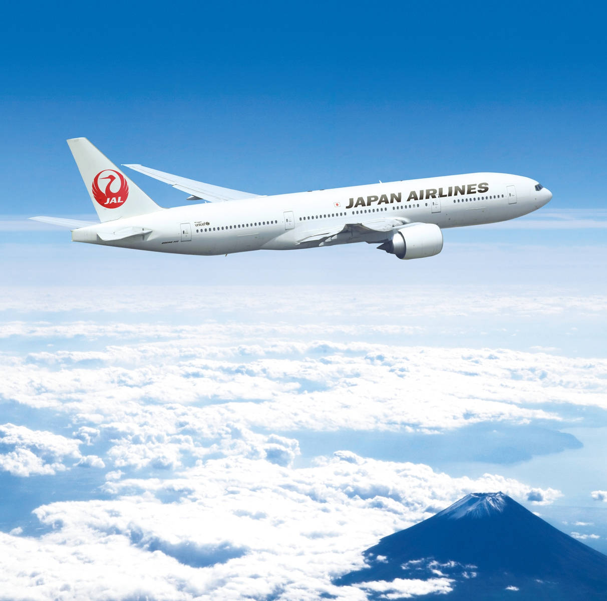 high 桌布 壁紙 — 日本航空的飛機在蓬鬆的白雲上方翱翔，下方可見富士山，天空清澈湛藍。